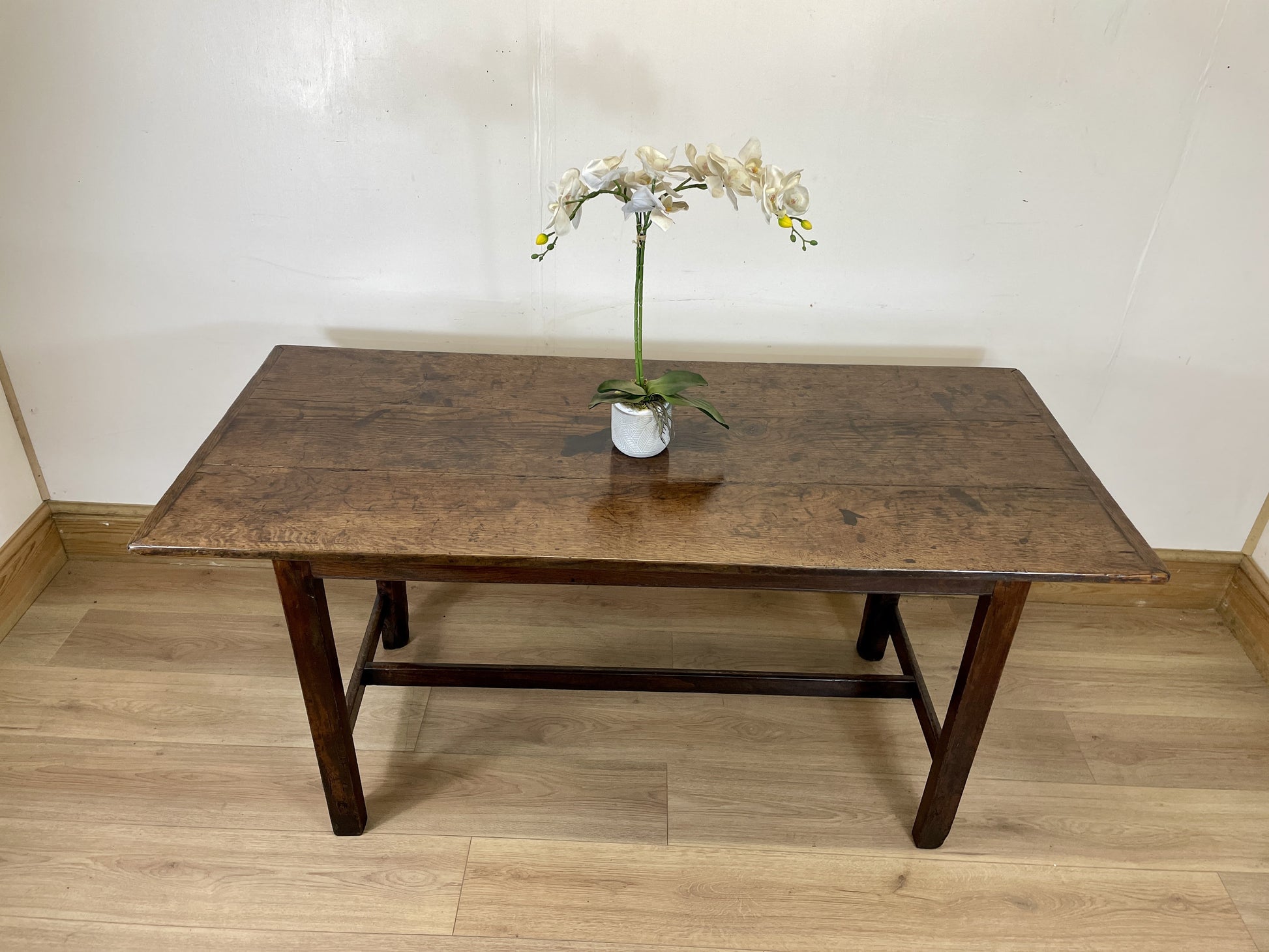 Wooden table with a vase of flowers on a wooden floor against a white wall