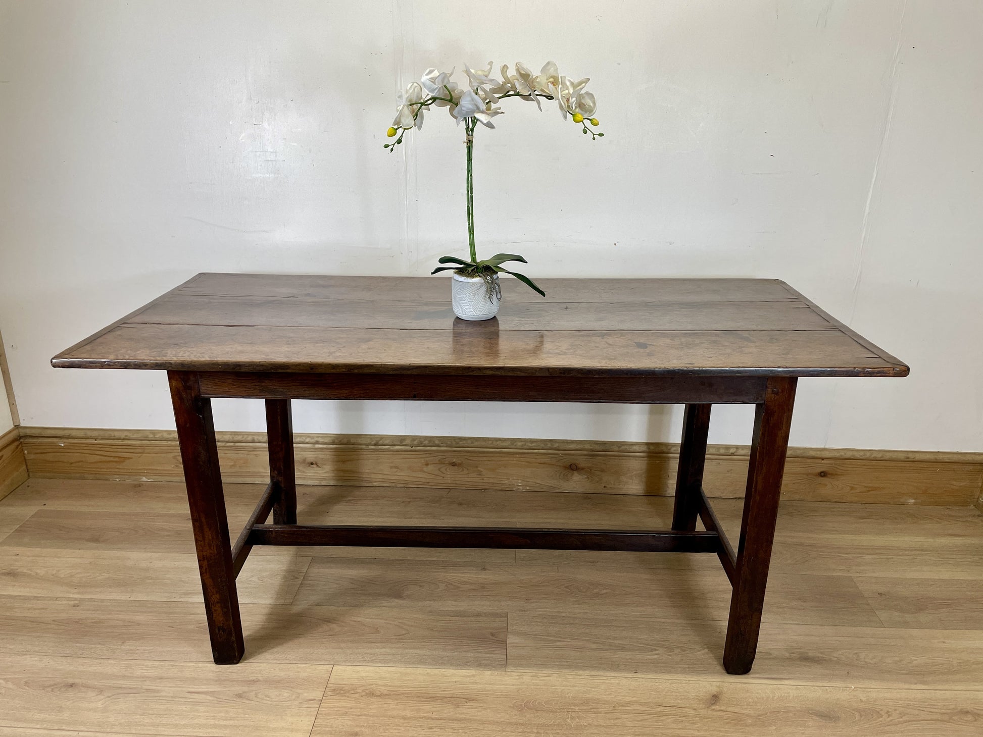 Wooden table with a vase of flowers on a wooden floor against a white wall