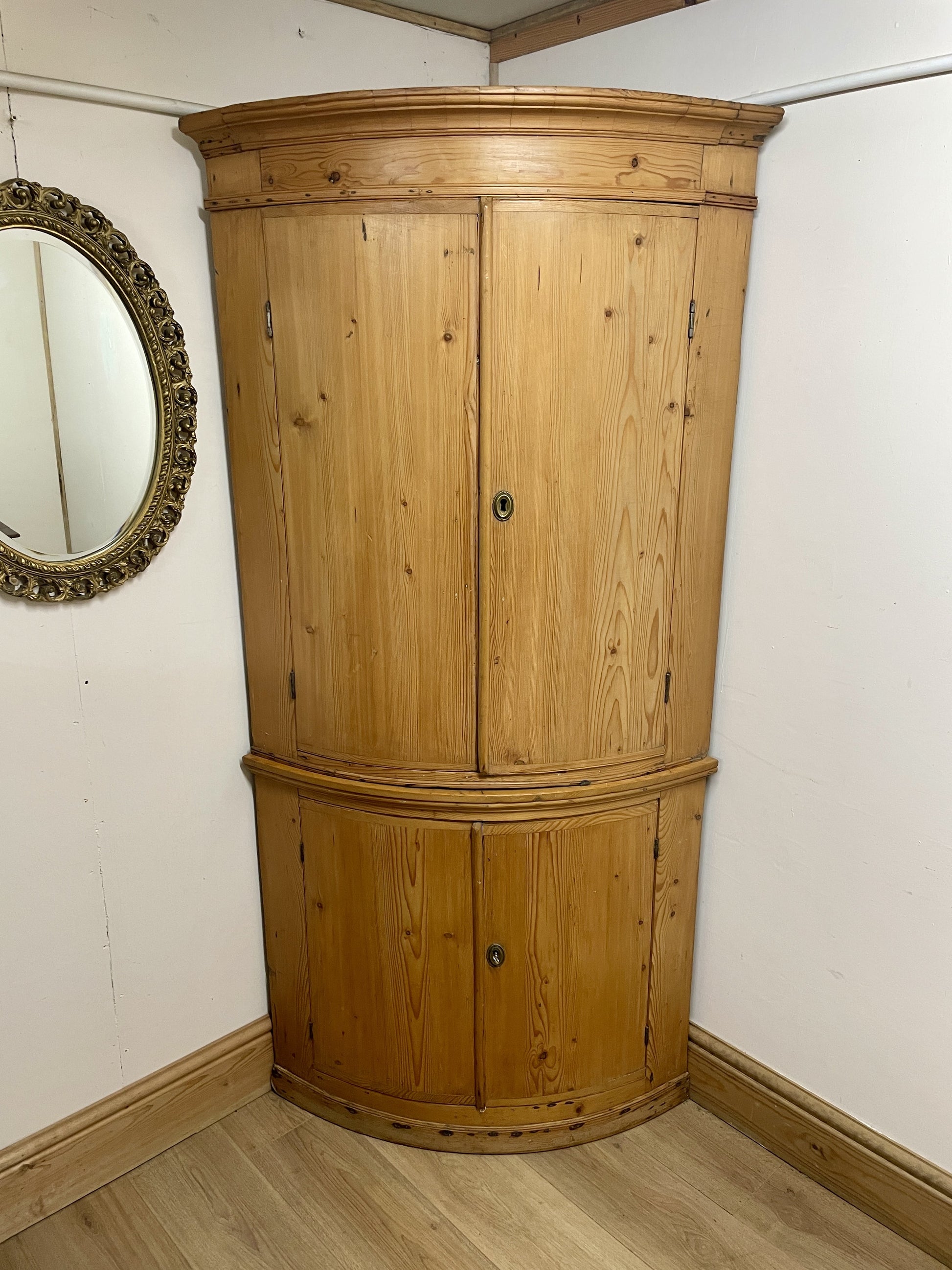 Wooden corner cabinet in a room with a mirror on the wall.