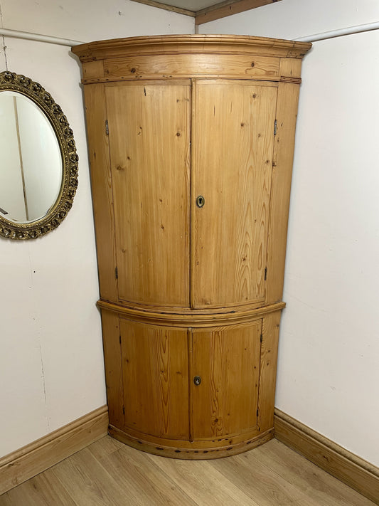 Wooden corner cabinet in a room with a mirror on the wall.