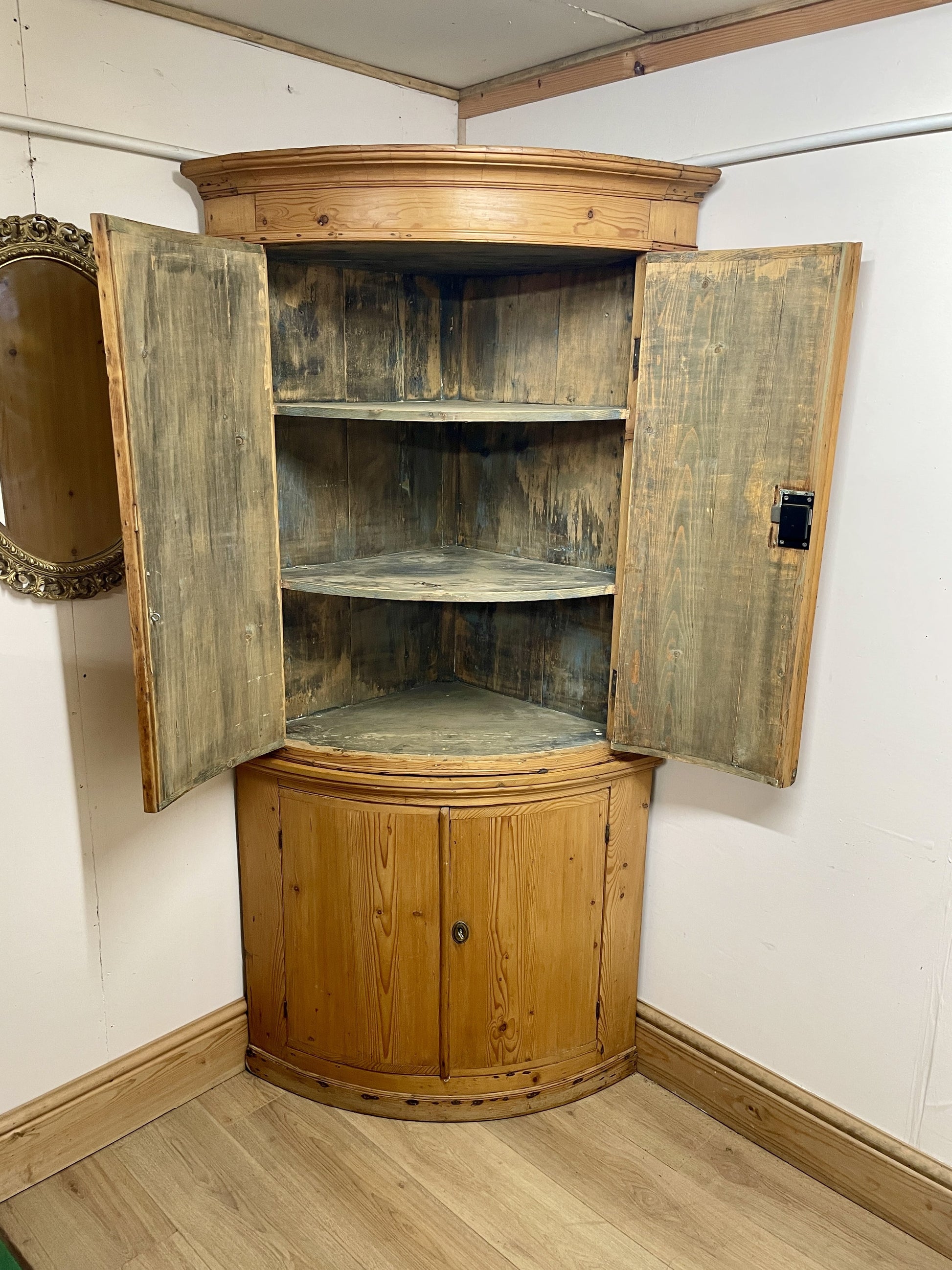 Wooden corner cabinet with open doors in a room with white walls and wooden floor.