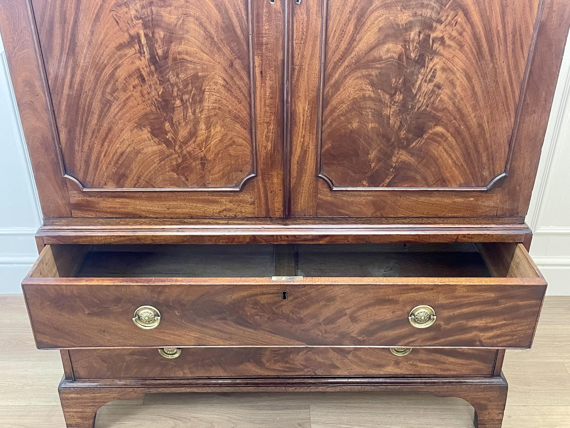 Wooden cabinet with two doors and a drawer on a wooden floor.