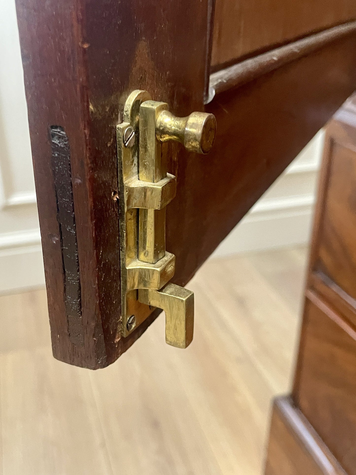 Close-up of a wooden cabinet with a brass latch on a light wood floor.