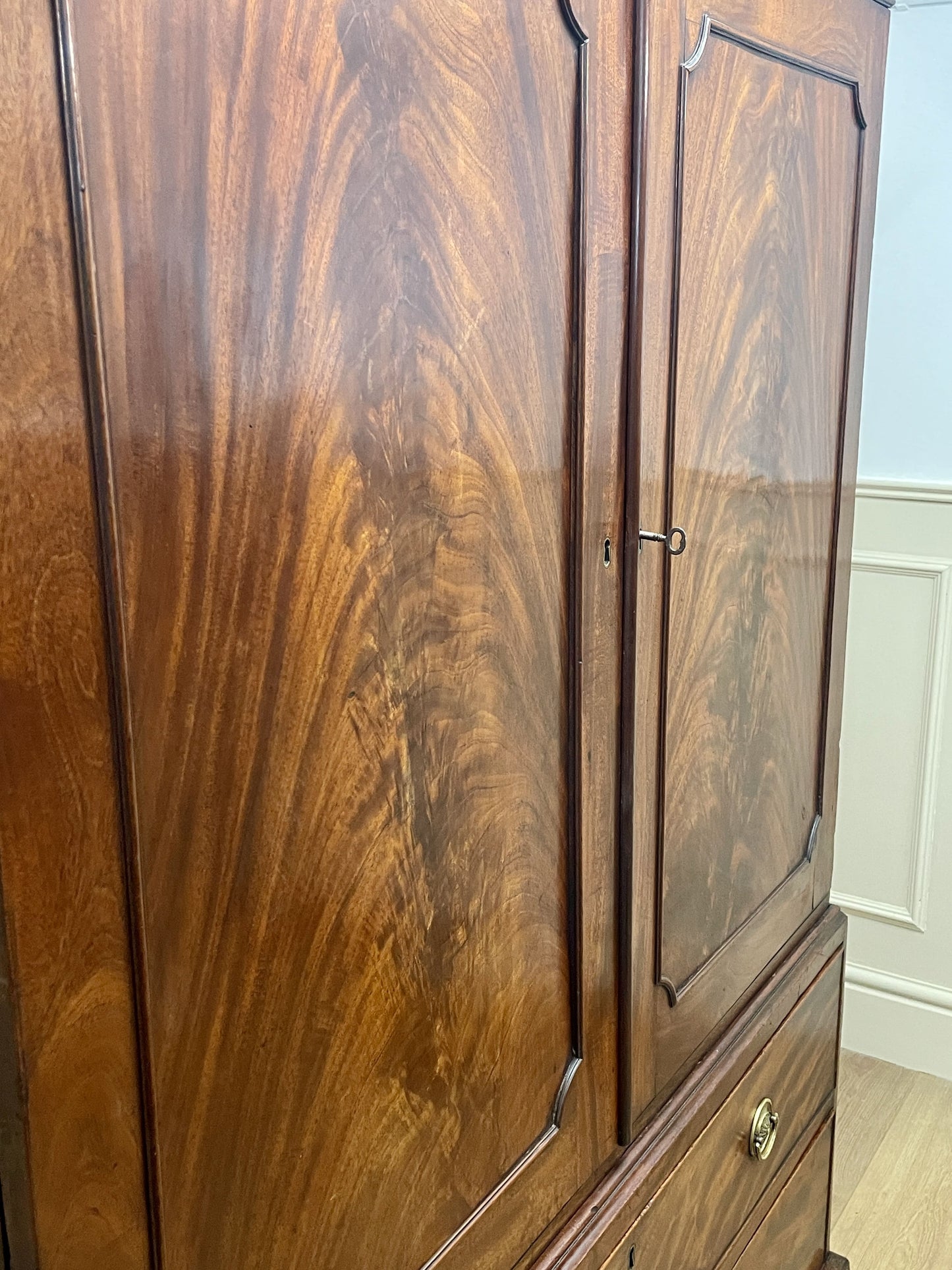 Wooden wardrobe with glass panel doors in a room with white walls and wooden floor.