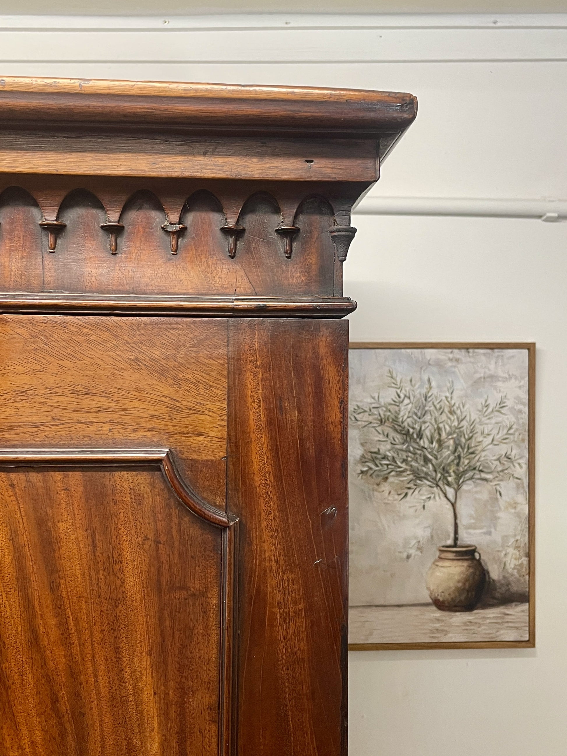 Wooden cabinet with decorative carvings next to a framed painting of a plant.