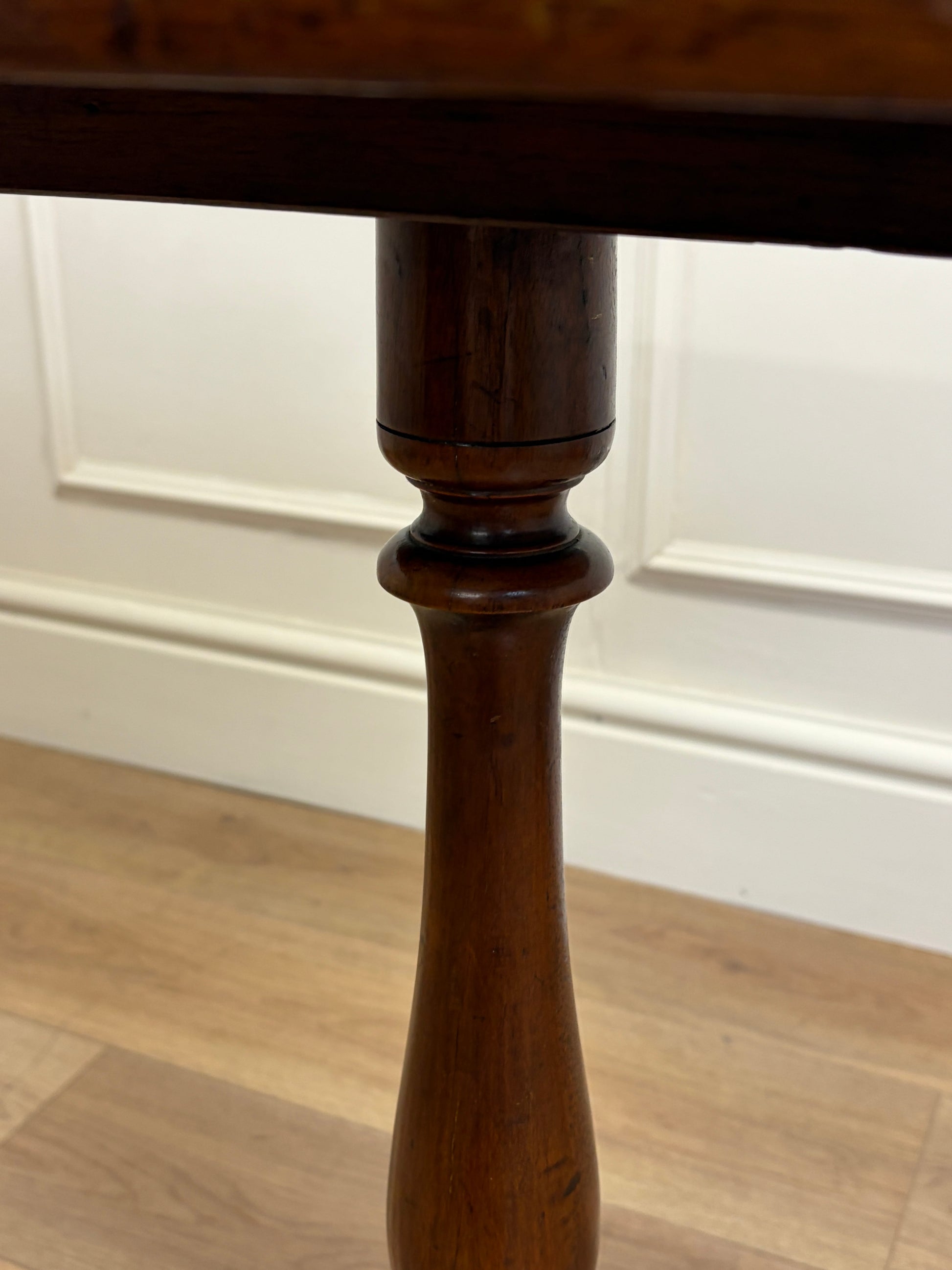 Close-up of a wooden table leg against a white paneled wall.