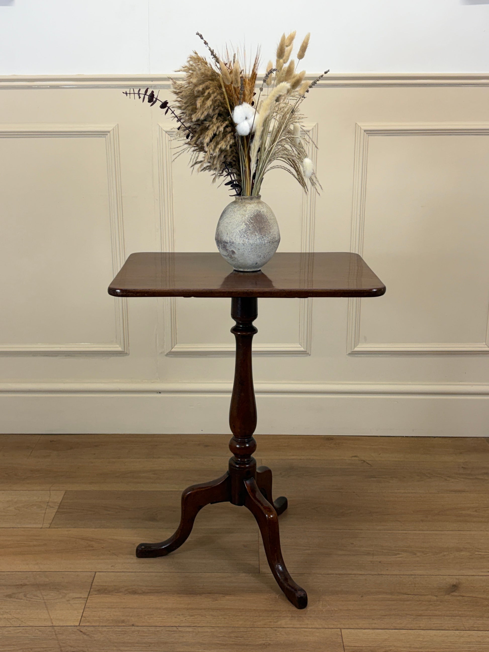 Wooden table with a vase of dried flowers against a paneled wall.