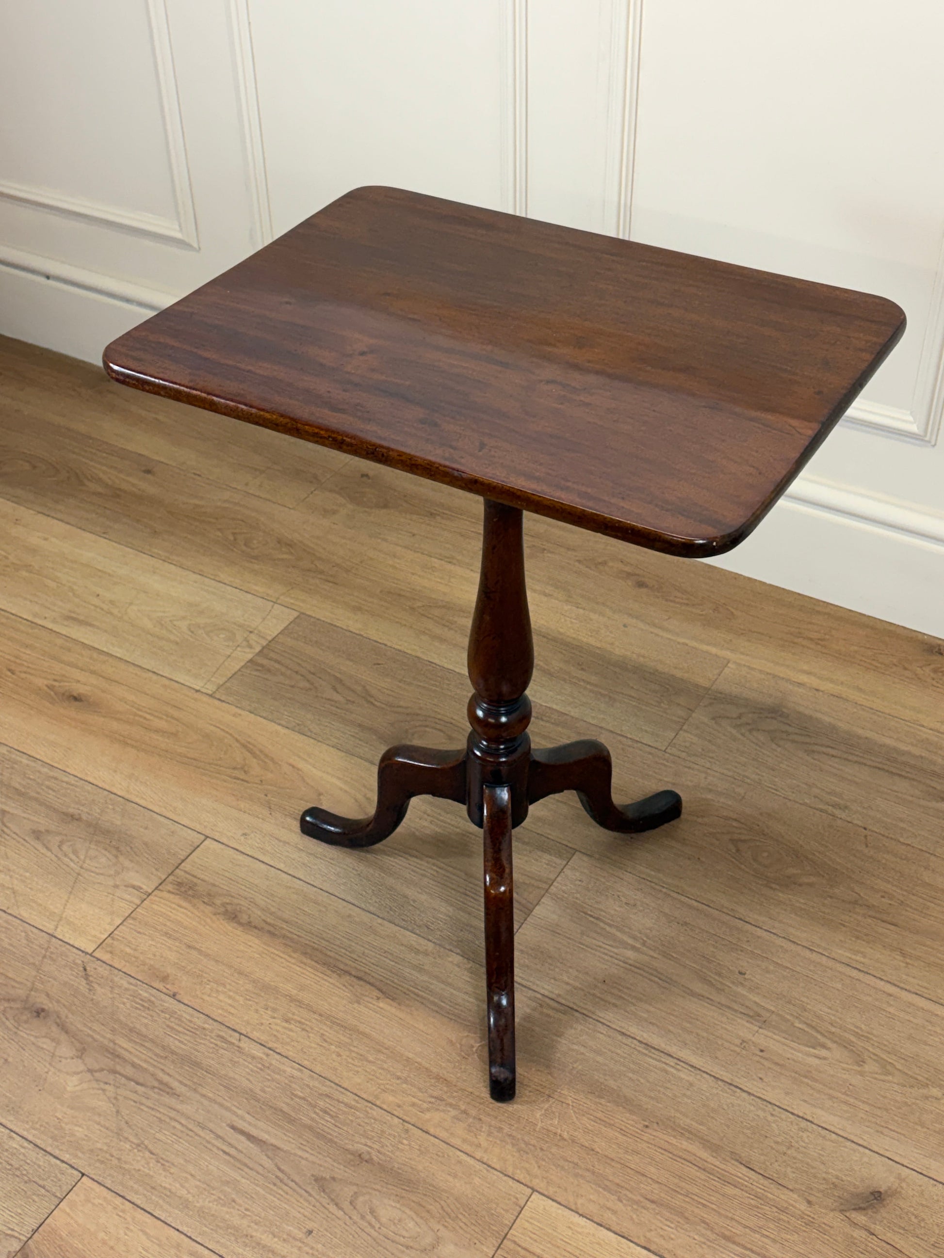 Wooden side table on a wooden floor with white paneled walls.