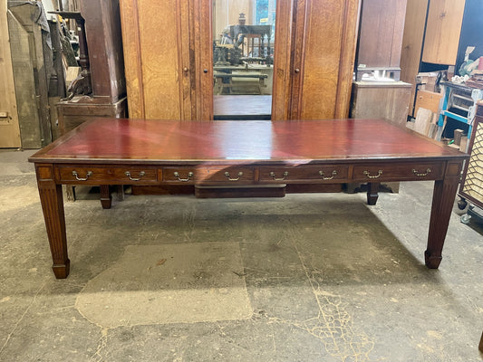 Large wooden dining table with multiple drawers in a storage or warehouse setting.