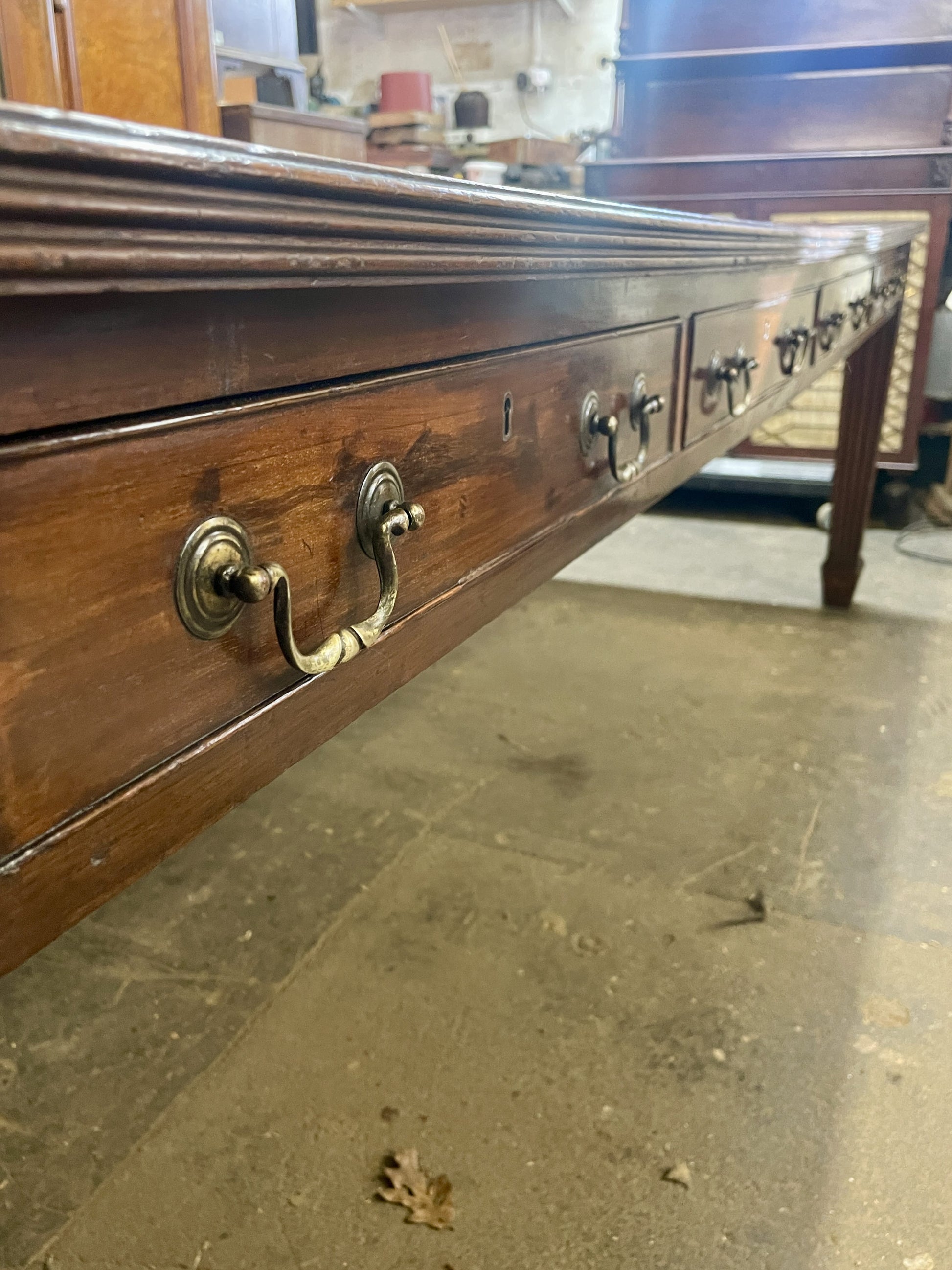 Long wooden drawer with brass handles on a stone floor.