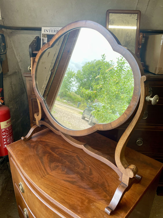 Wooden vanity mirror with a reflective surface on a wooden dresser.