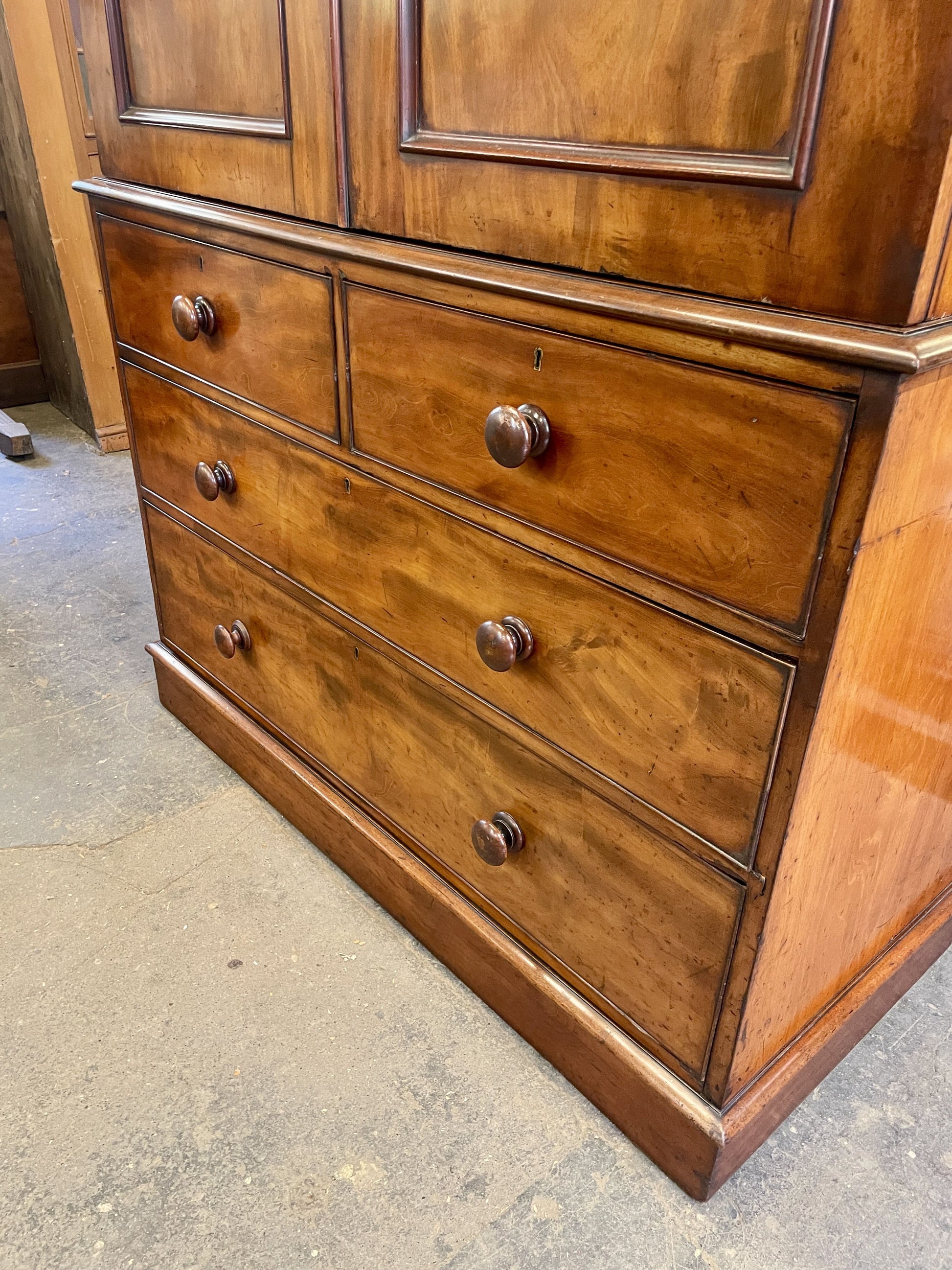 Wooden dresser with multiple drawers and a door on a concrete floor.