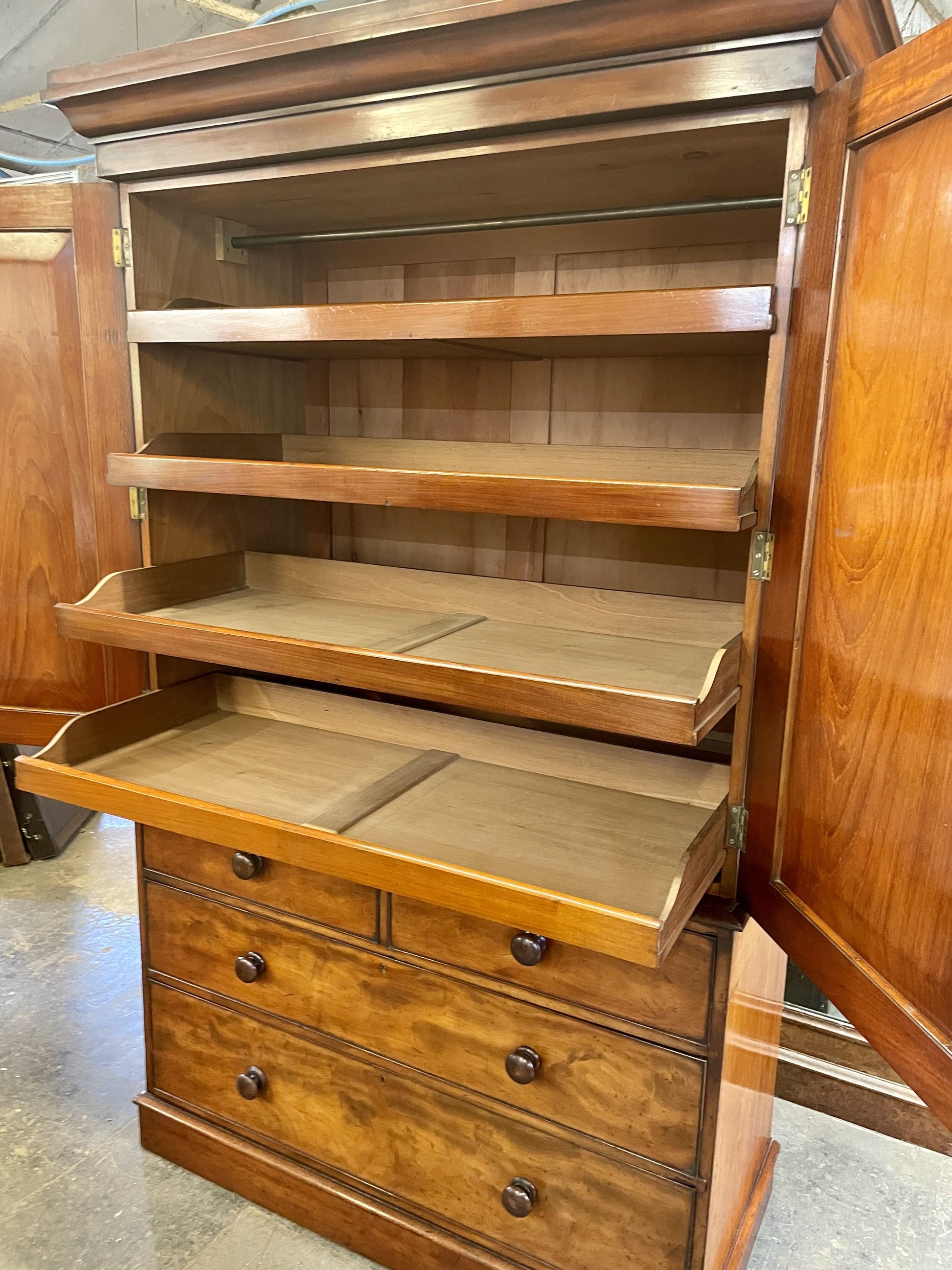 Wooden cabinet with open doors and drawers on a concrete floor.
