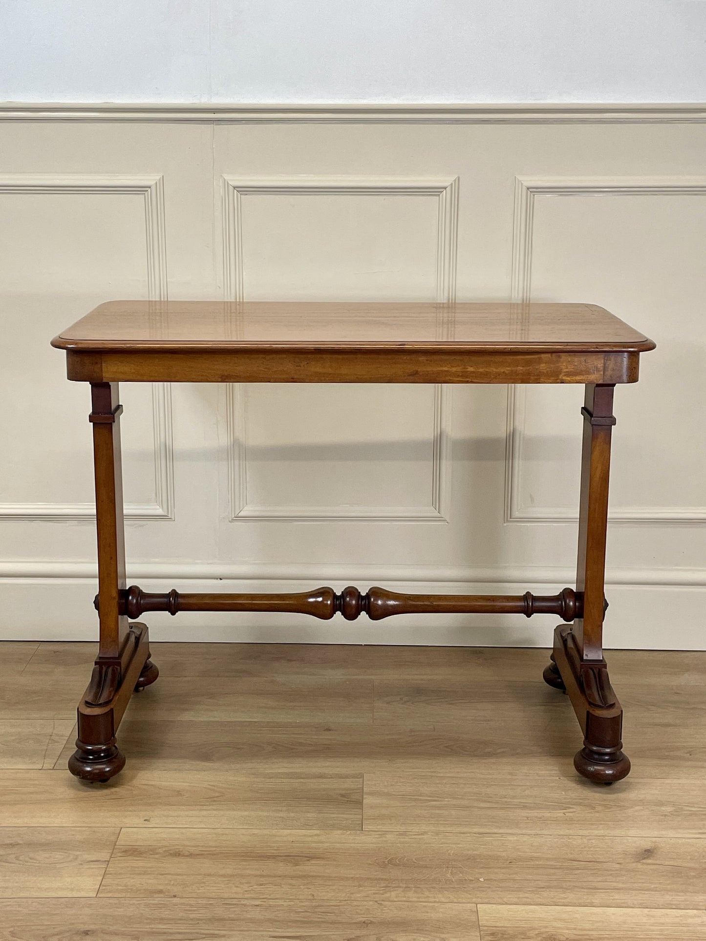 Wooden table with a classical design against a white paneled wall.