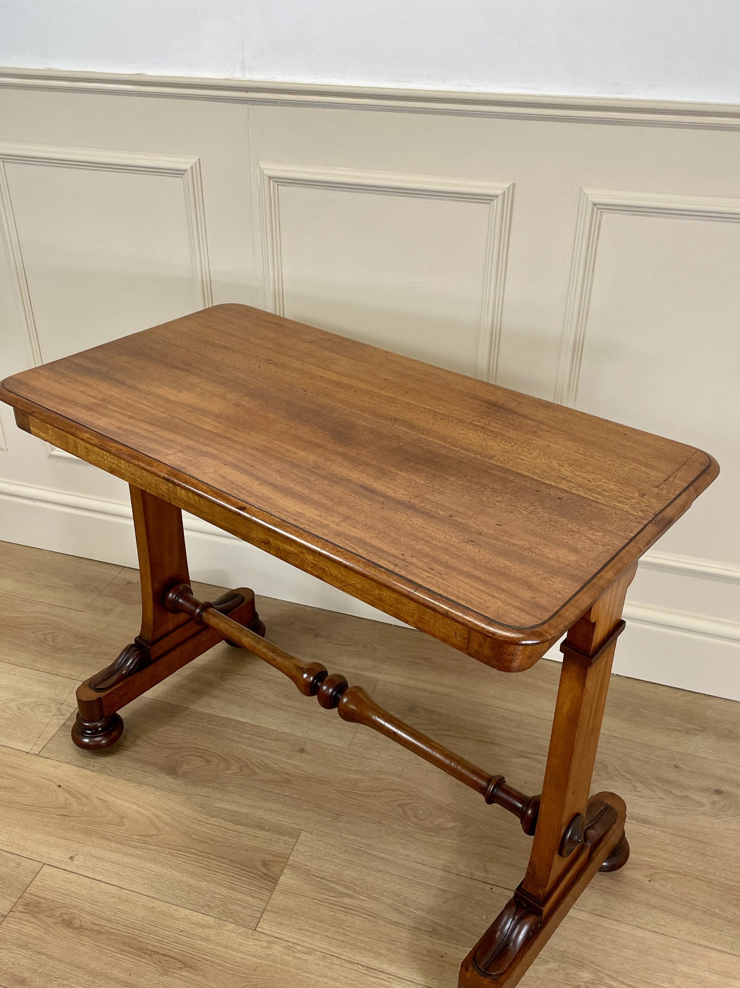 Wooden table with a curved leg design on a wooden floor against a white paneled wall.