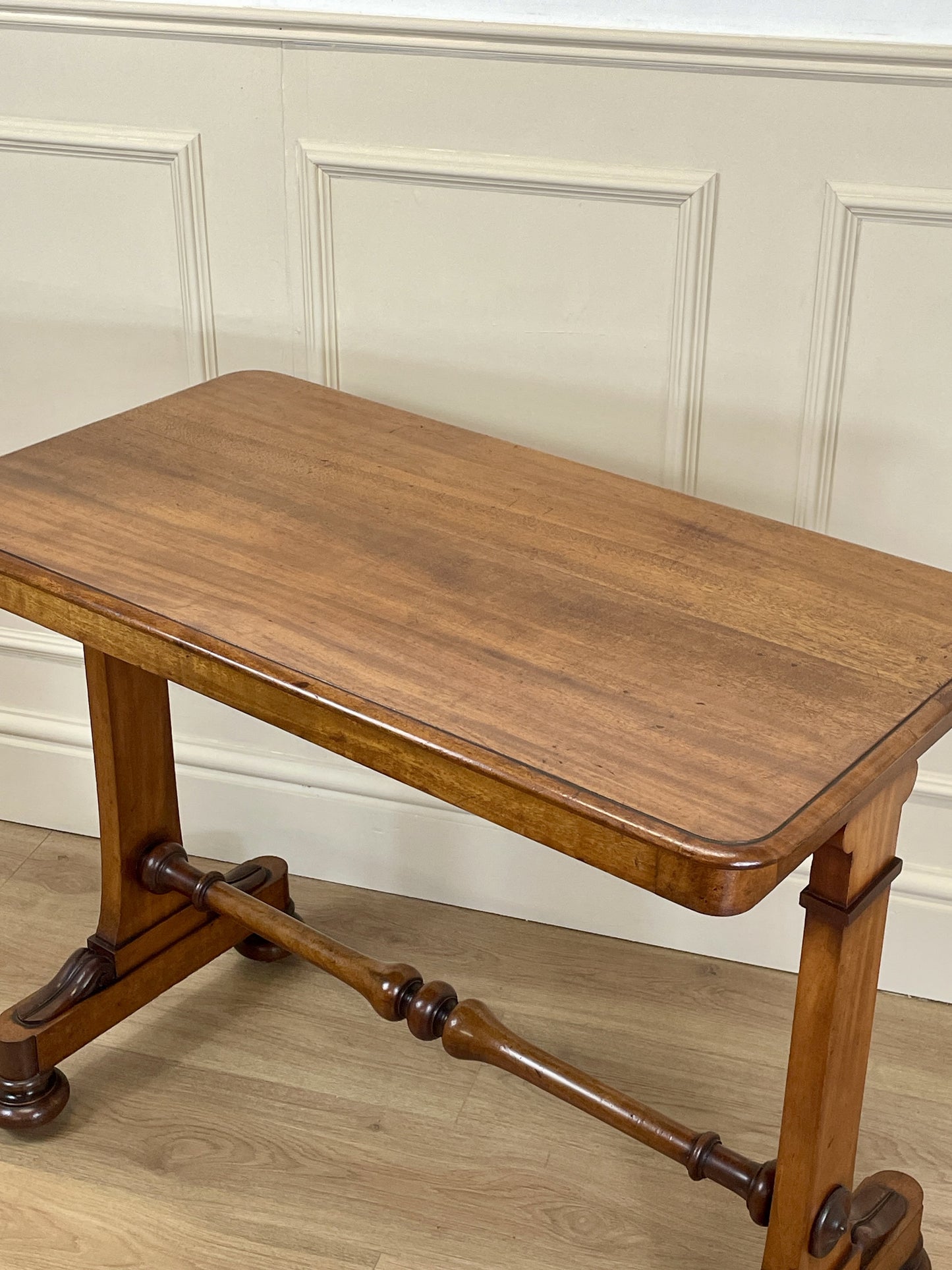 Wooden table with a classical design against a white paneled wall.