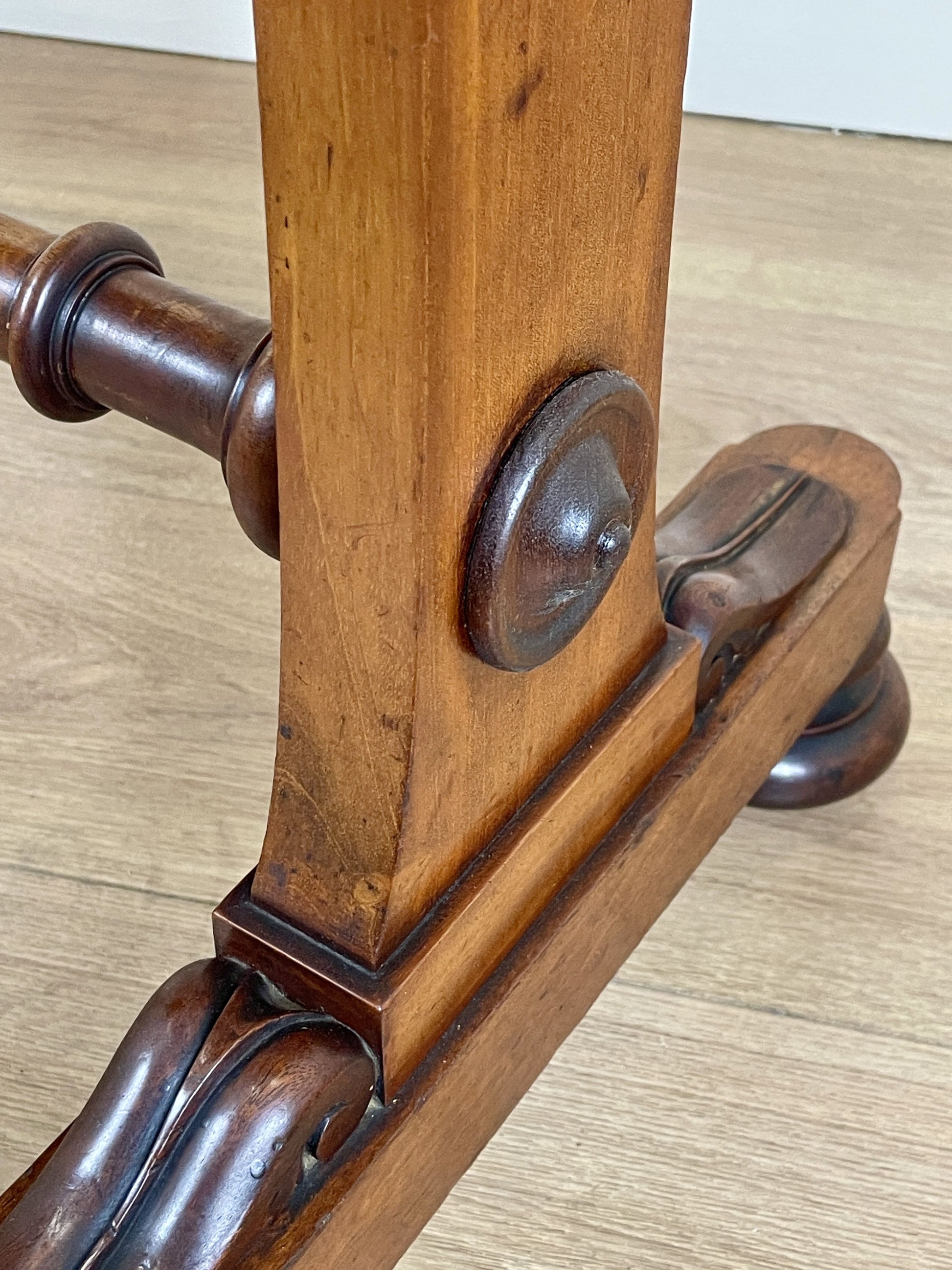 Close-up of a wooden garment rack with metal brackets on a light wood floor.