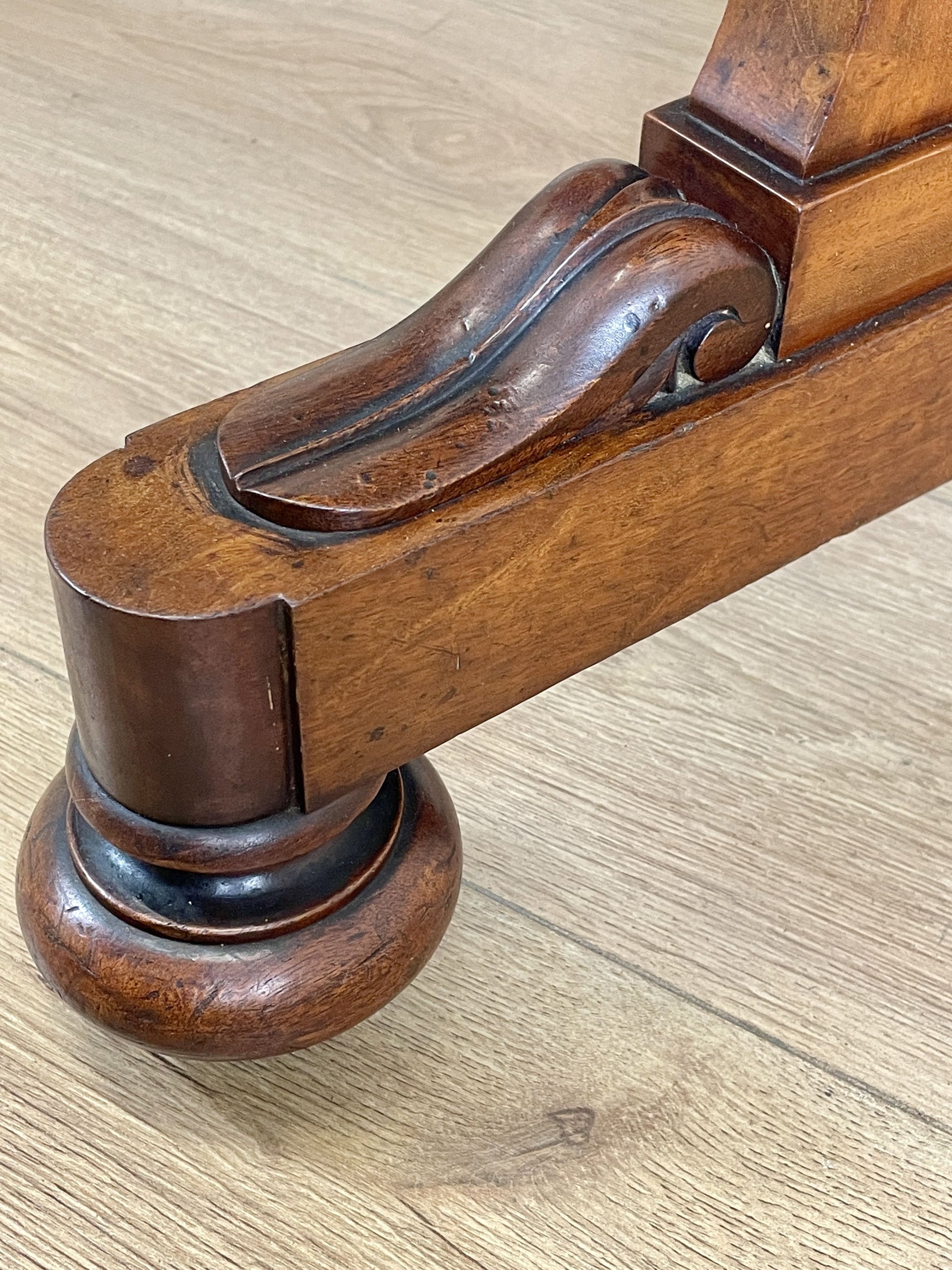 Wooden furniture leg with decorative carvings on a wooden floor.