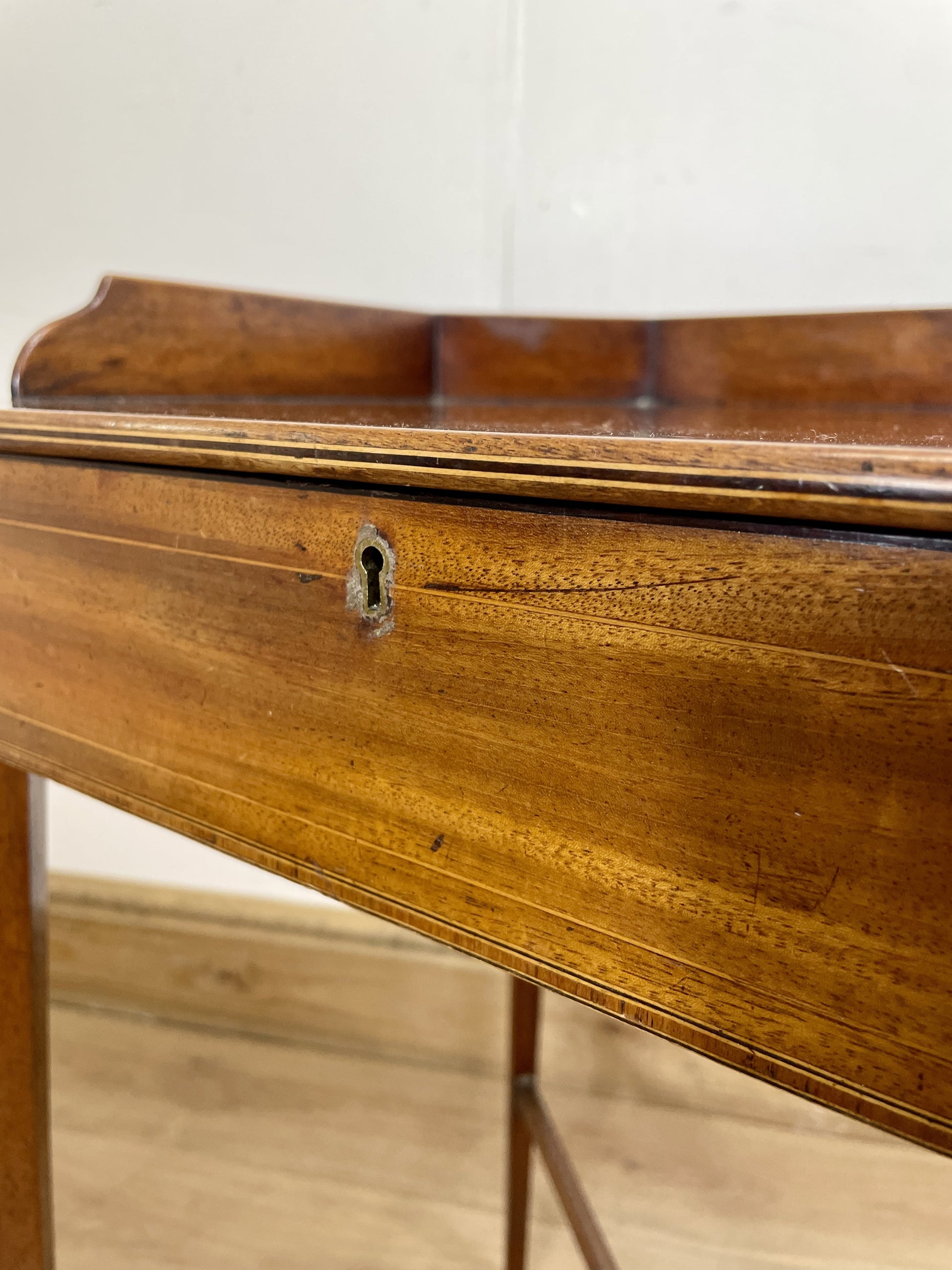 Close-up of a wooden desk with a keyhole on a light wood floor.