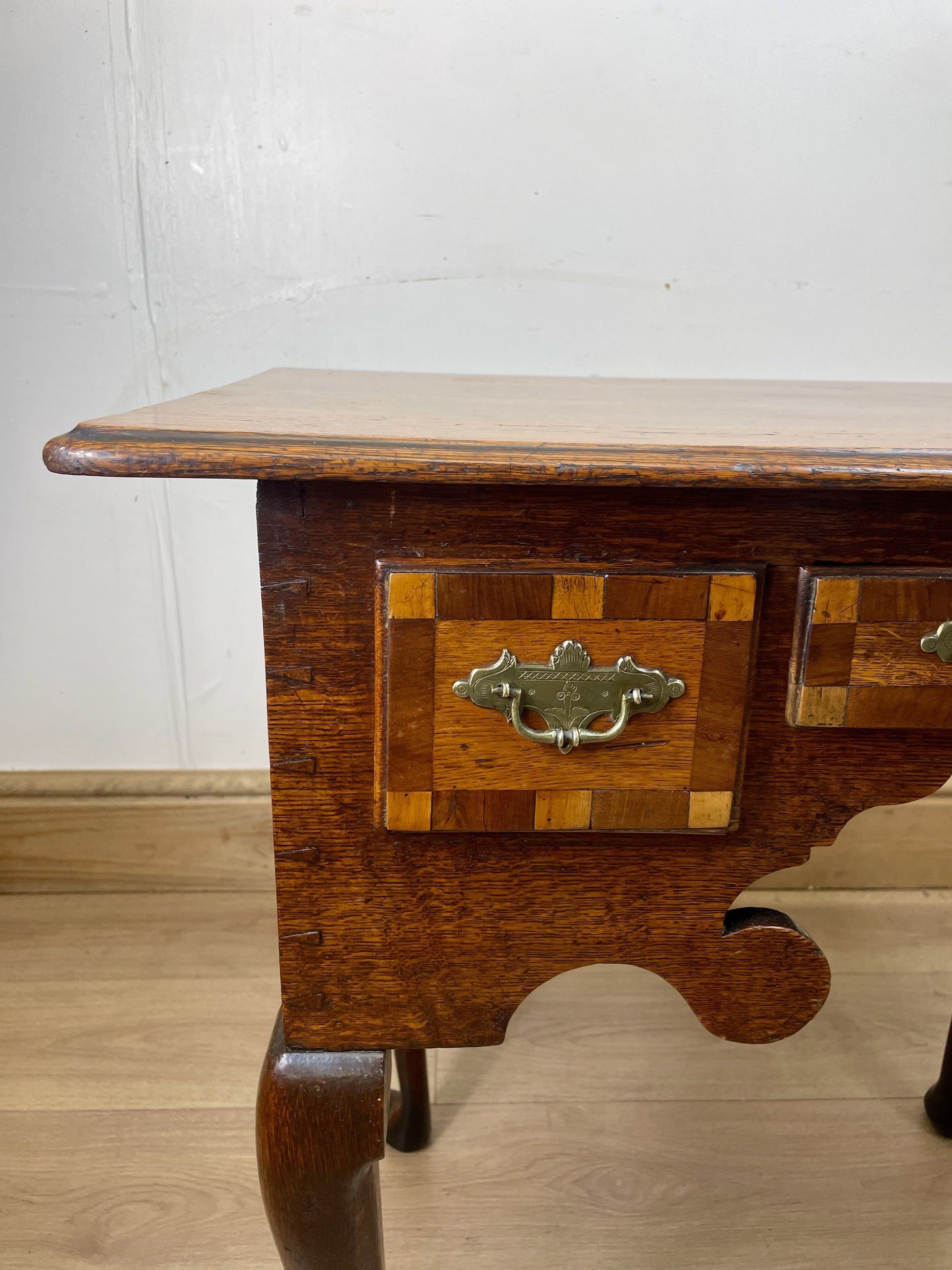Wooden side table with a checkered pattern and brass handle on a wooden floor.