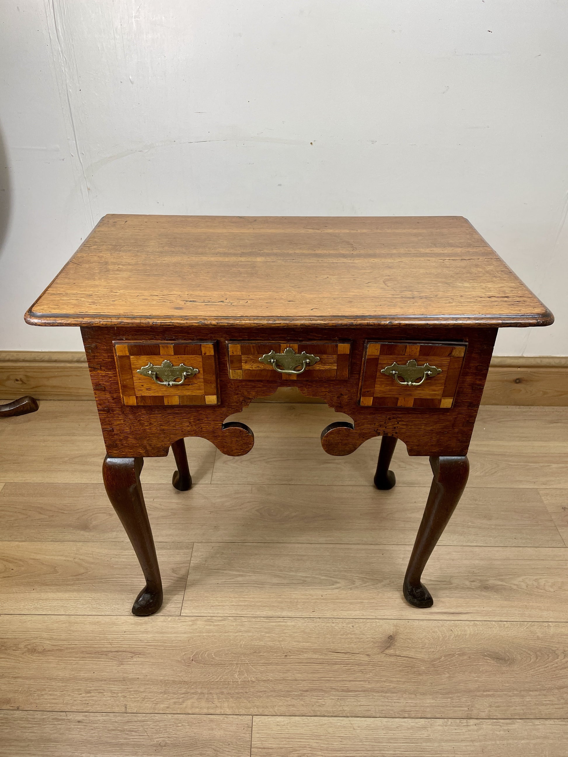 Wooden side table with two drawers on a wooden floor against a white wall
