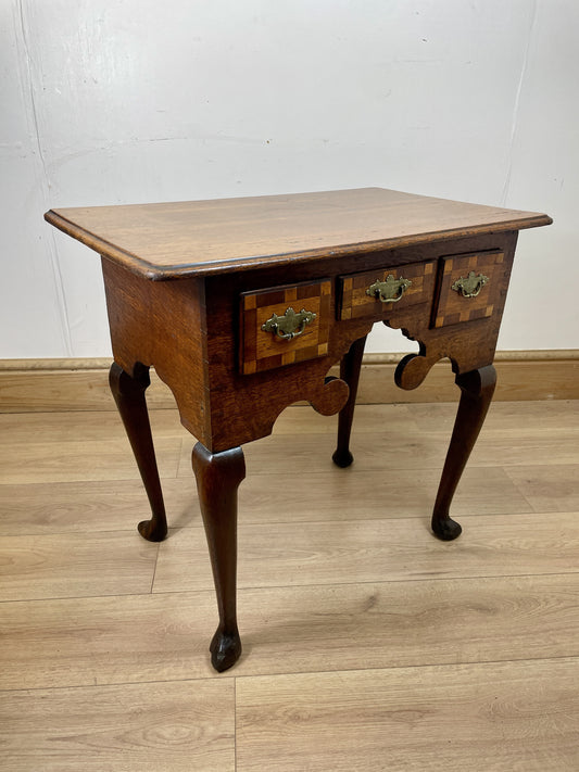 Wooden side table with two drawers on a wooden floor against a white wall