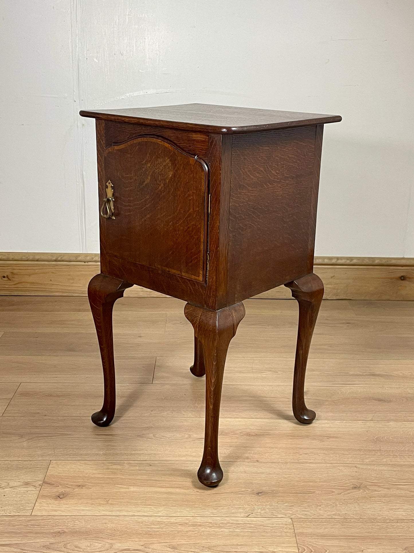 Wooden side table with curved legs on a wooden floor against a white wall