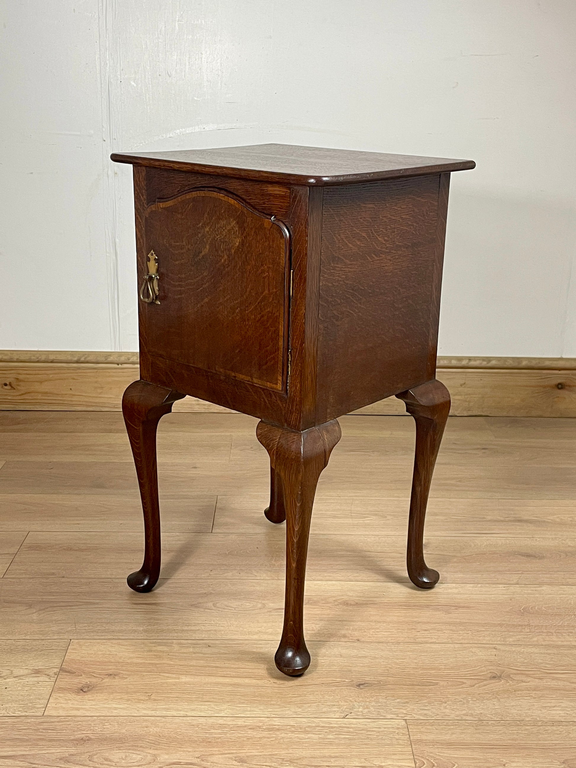 Wooden side table with curved legs on a wooden floor against a white wall