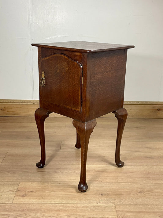 Wooden side table with curved legs on a wooden floor against a white wall
