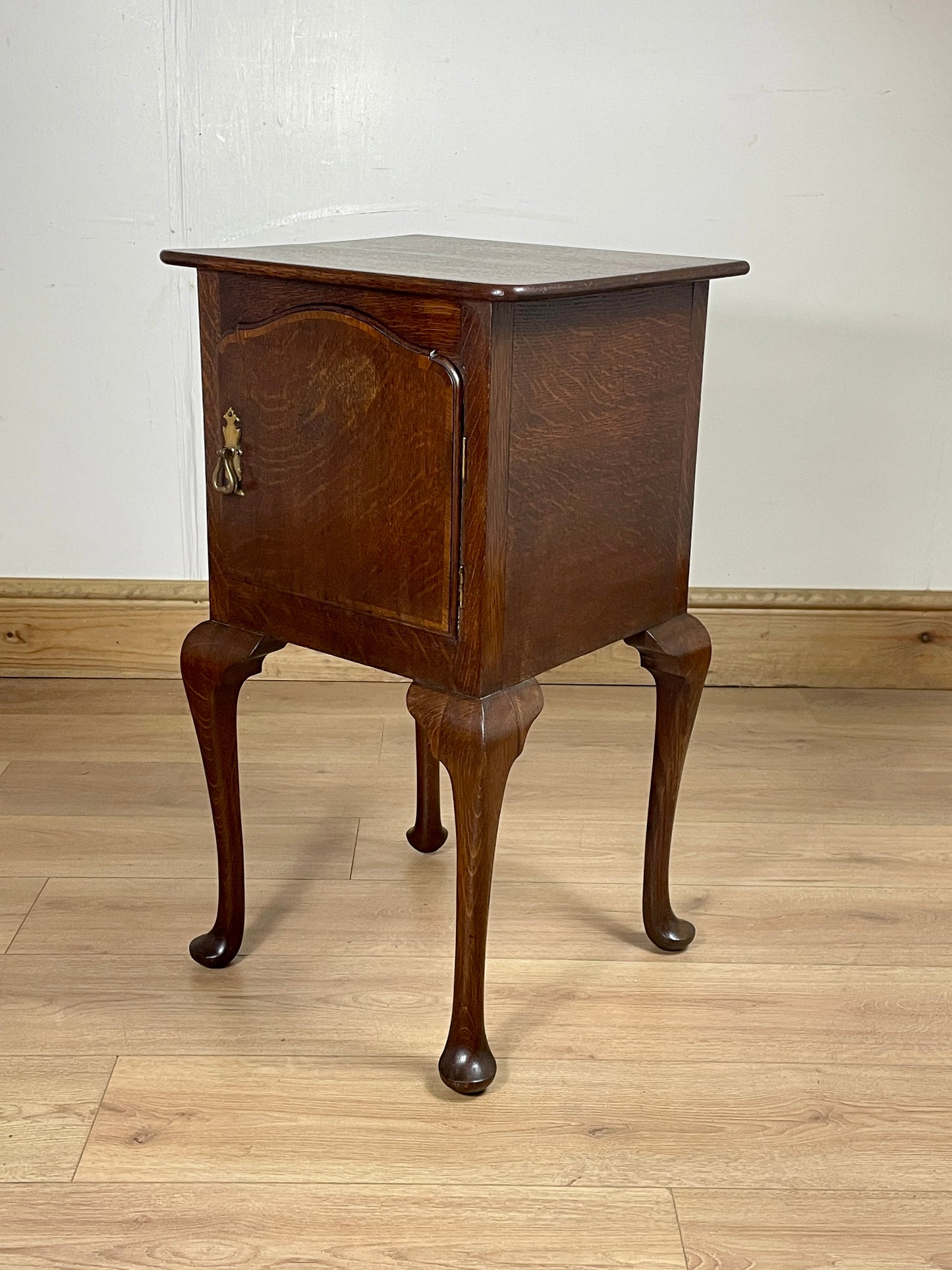 Wooden side table with curved legs on a wooden floor against a white wall