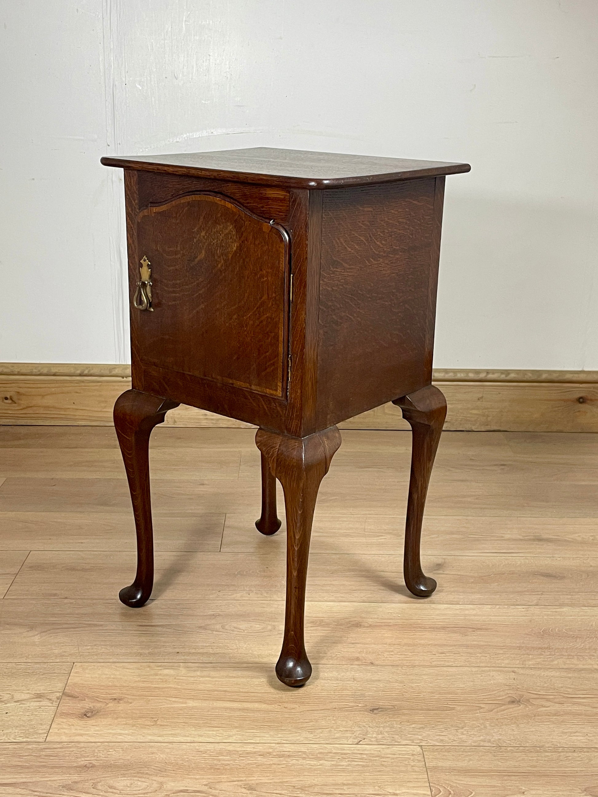 Wooden side table with curved legs on a wooden floor against a white wall