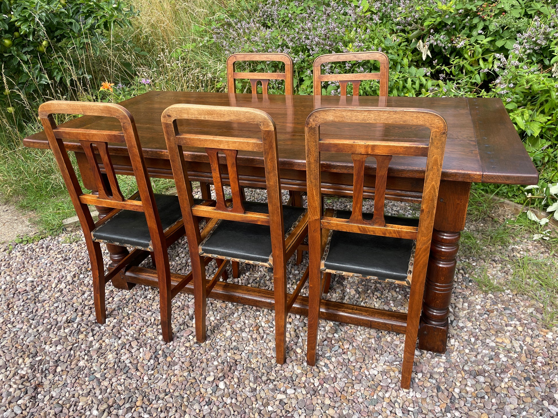 Wooden dining table with six matching chairs outdoors on a gravel surface.