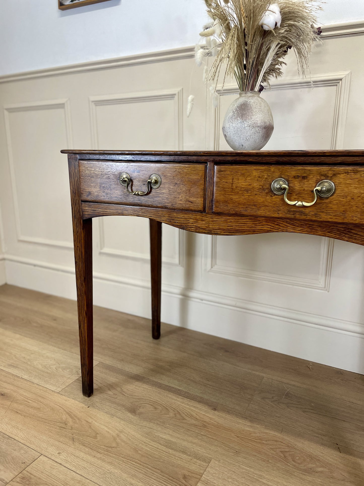 Wooden console table with two drawers against a white paneled wall.