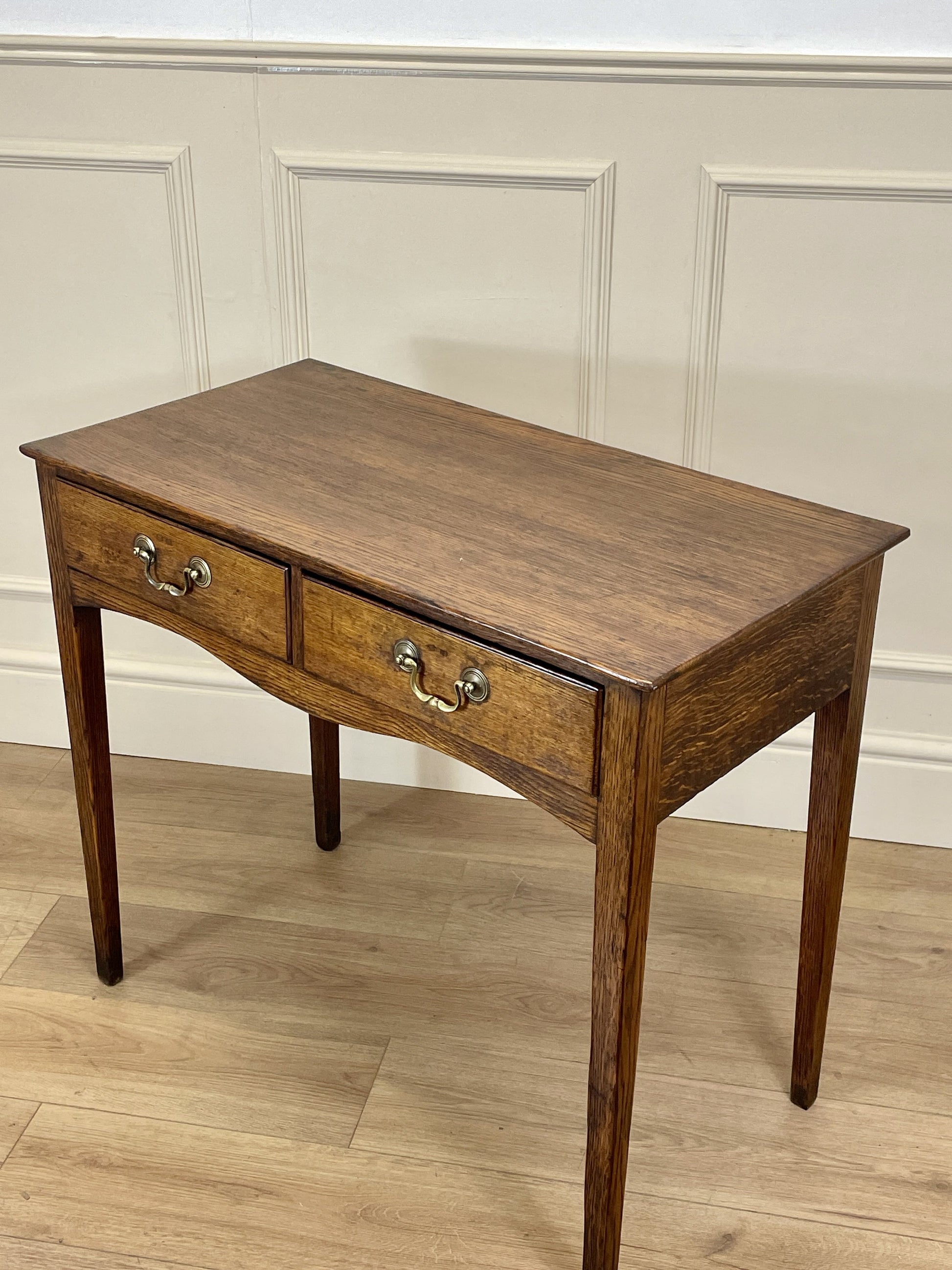 Wooden side table with two drawers against a paneled wall.