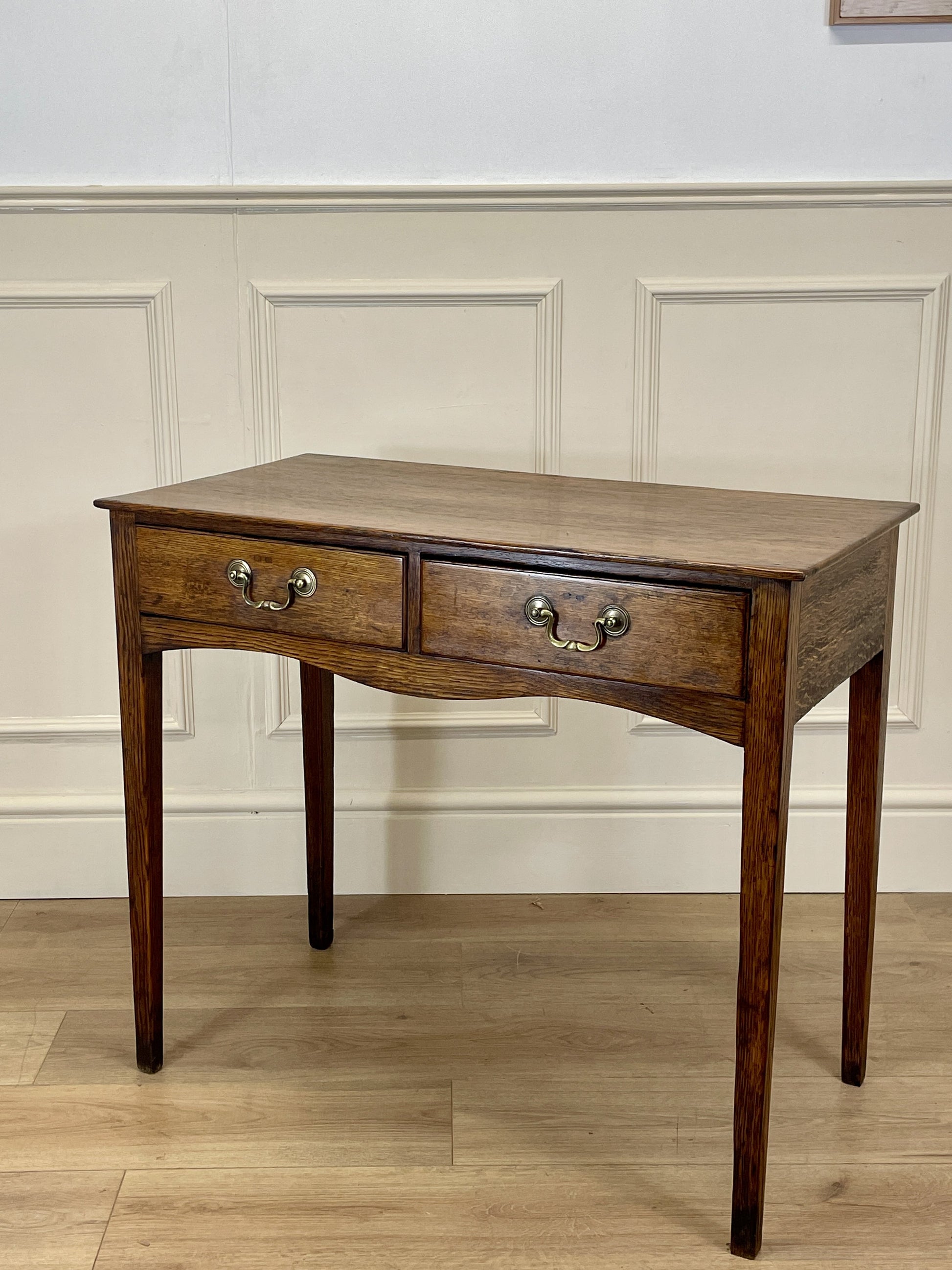 Wooden desk with two drawers against a white paneled wall.