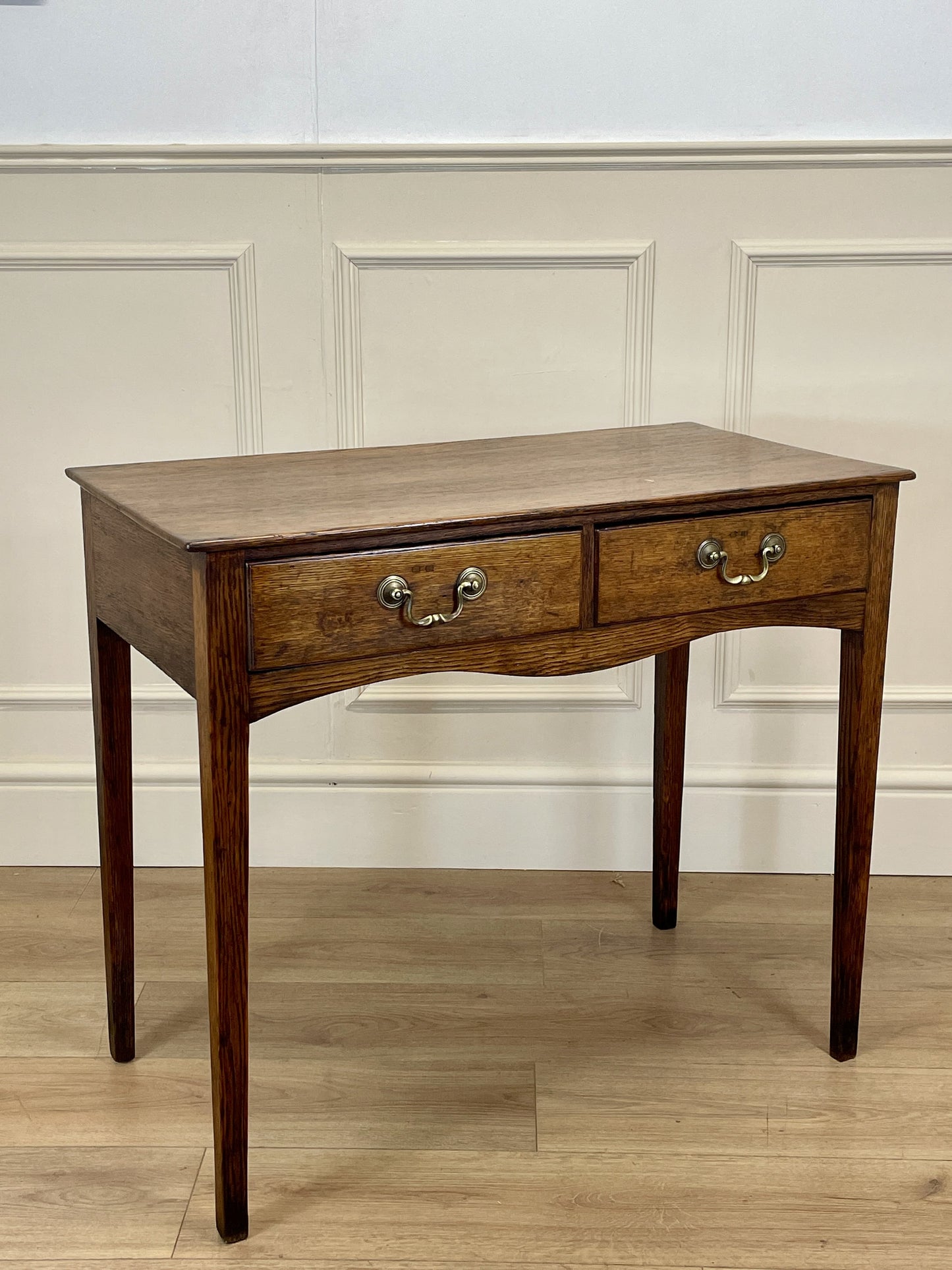 Wooden desk with two drawers against a paneled wall.
