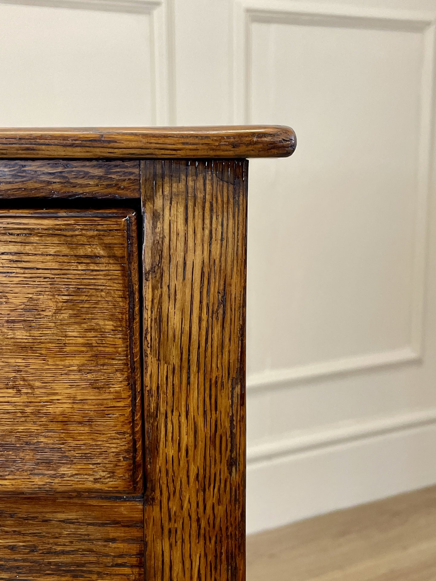 Close-up of a wooden cabinet corner with a white paneled wall in the background