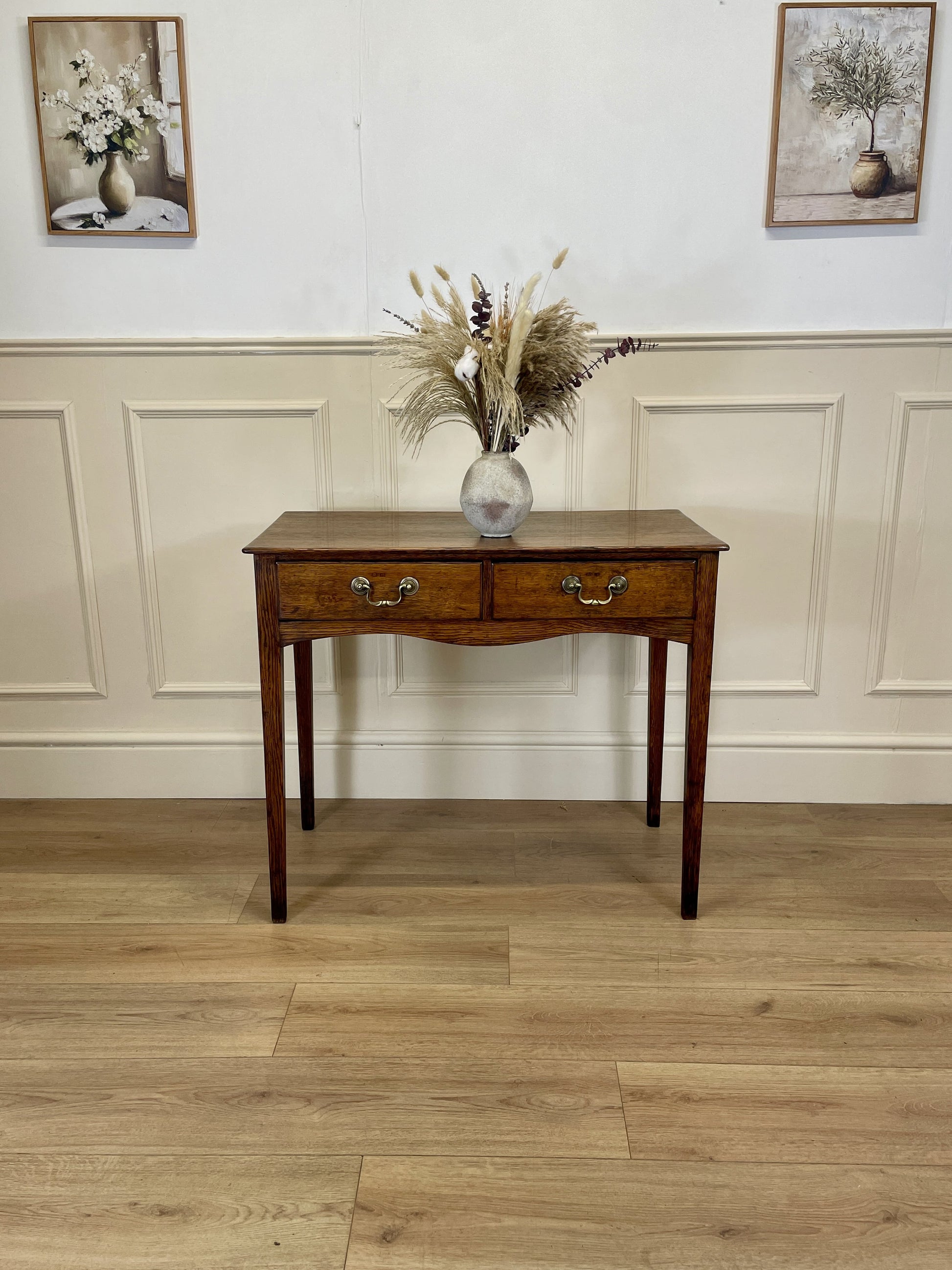 Wooden console table with a vase of flowers on a wooden floor with white walls.