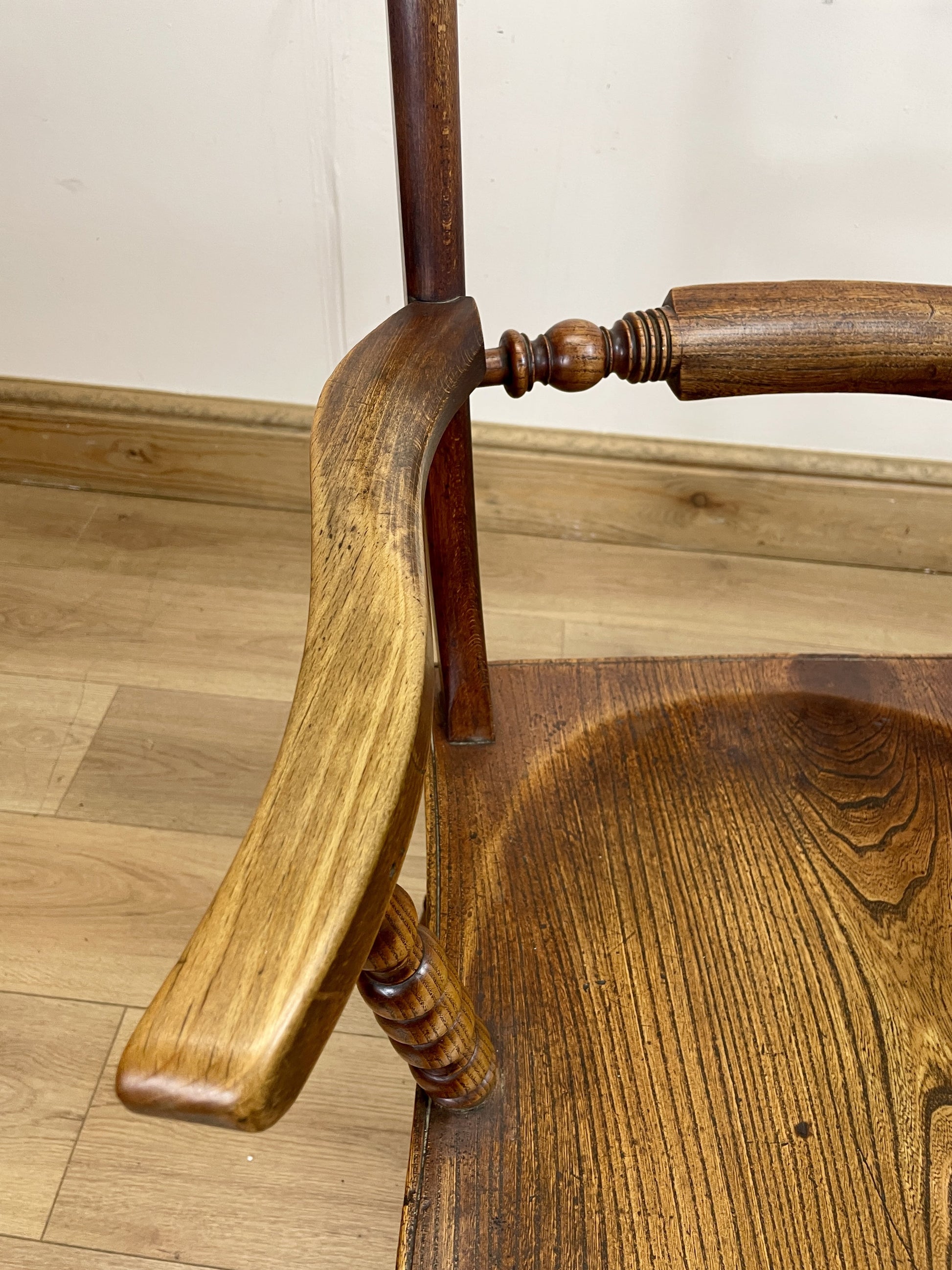 Close-up of a wooden chair with a focus on the armrest and seat.