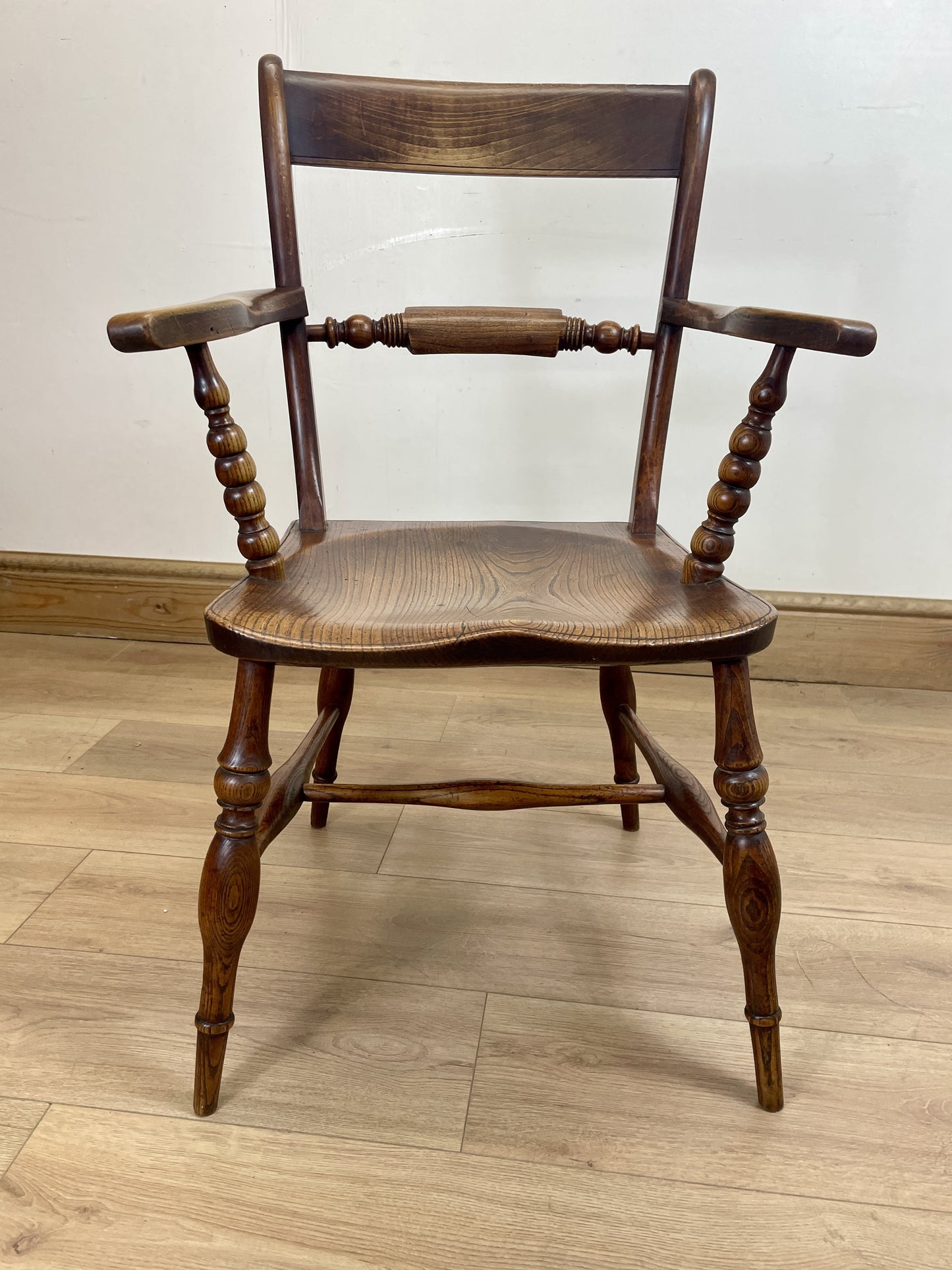 Wooden chair with armrests on a wooden floor against a white wall