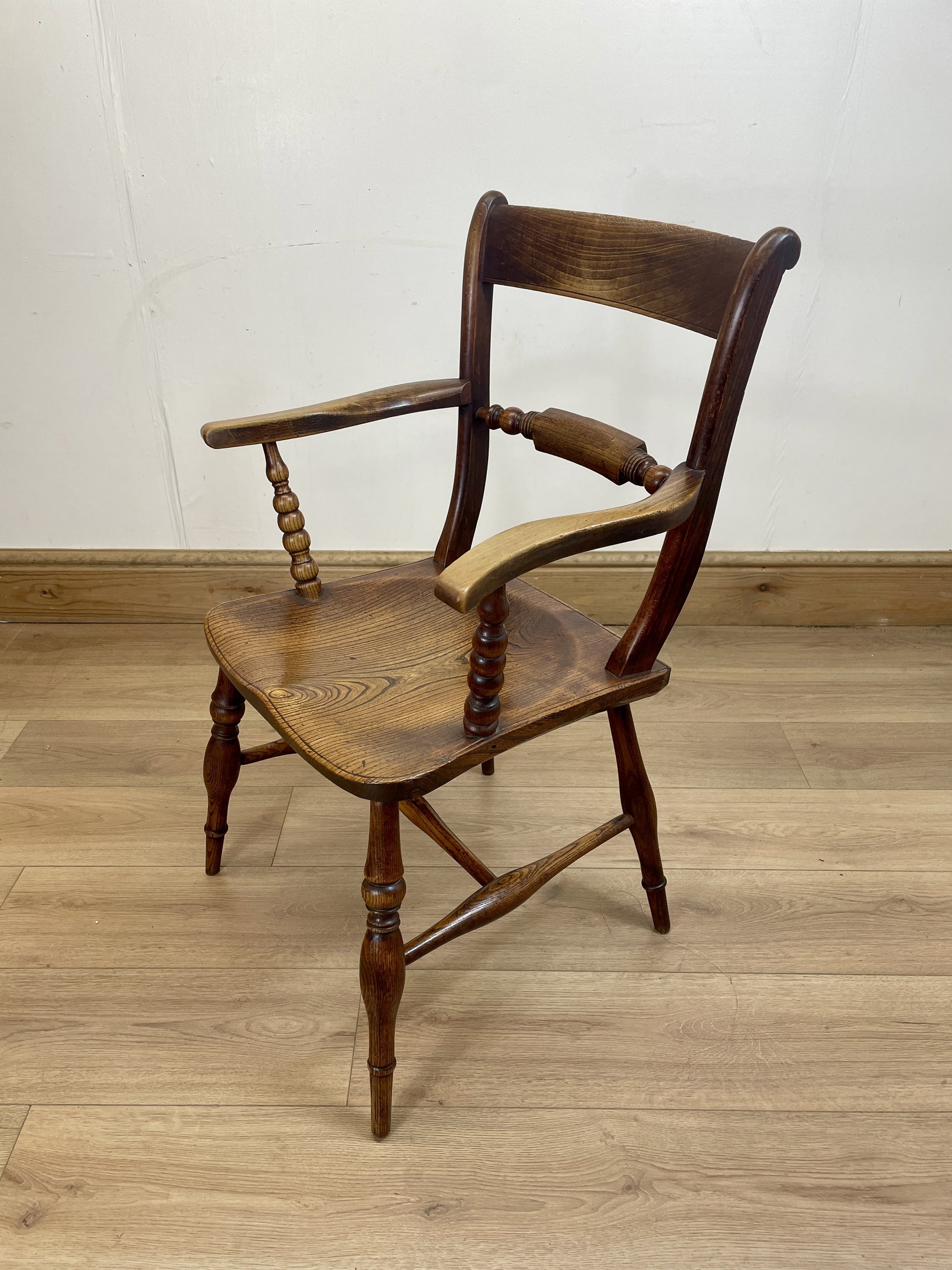 Wooden chair with armrests on a wooden floor against a white wall