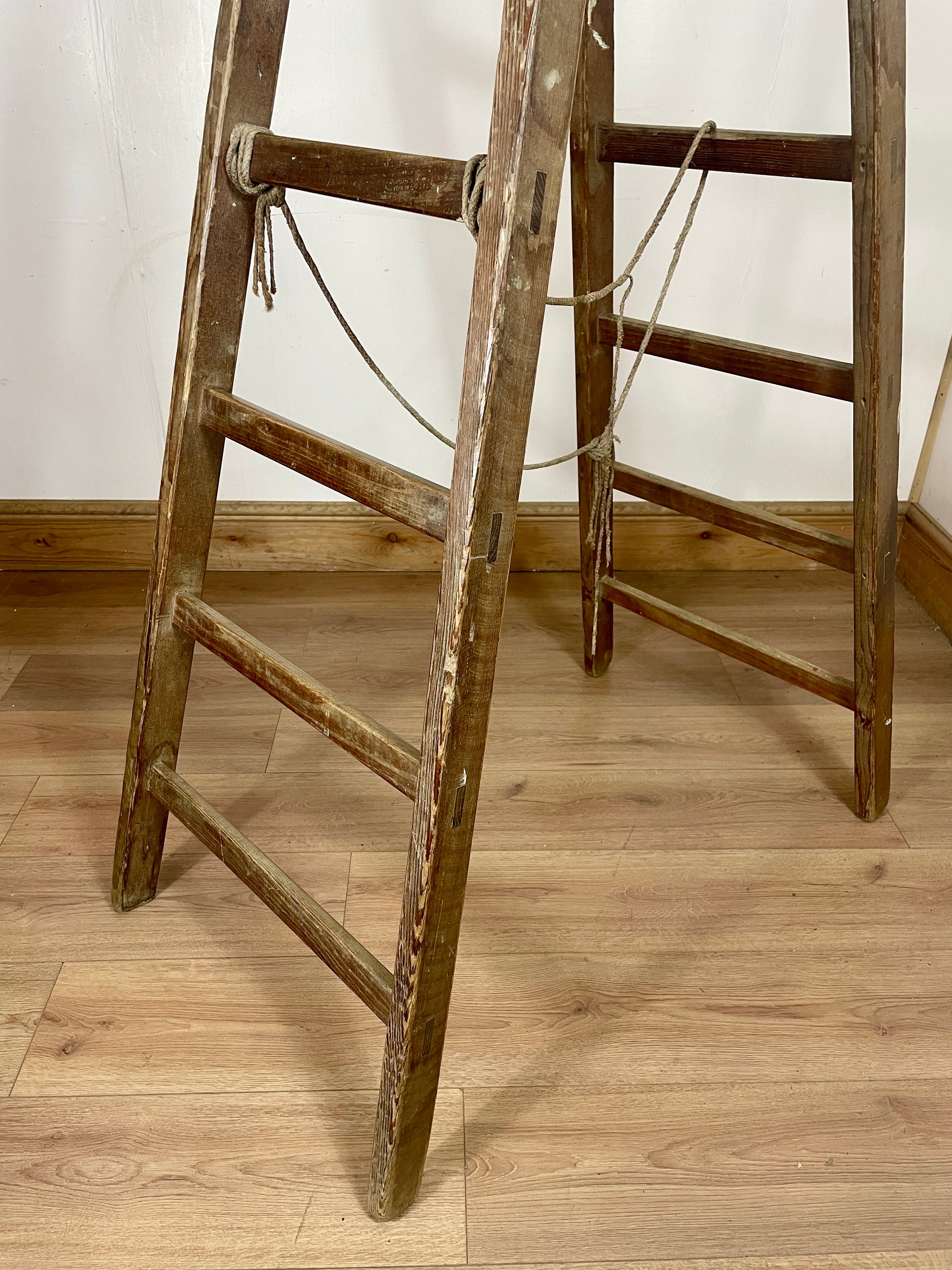 Wooden ladders leaning against a white wall on a wooden floor.