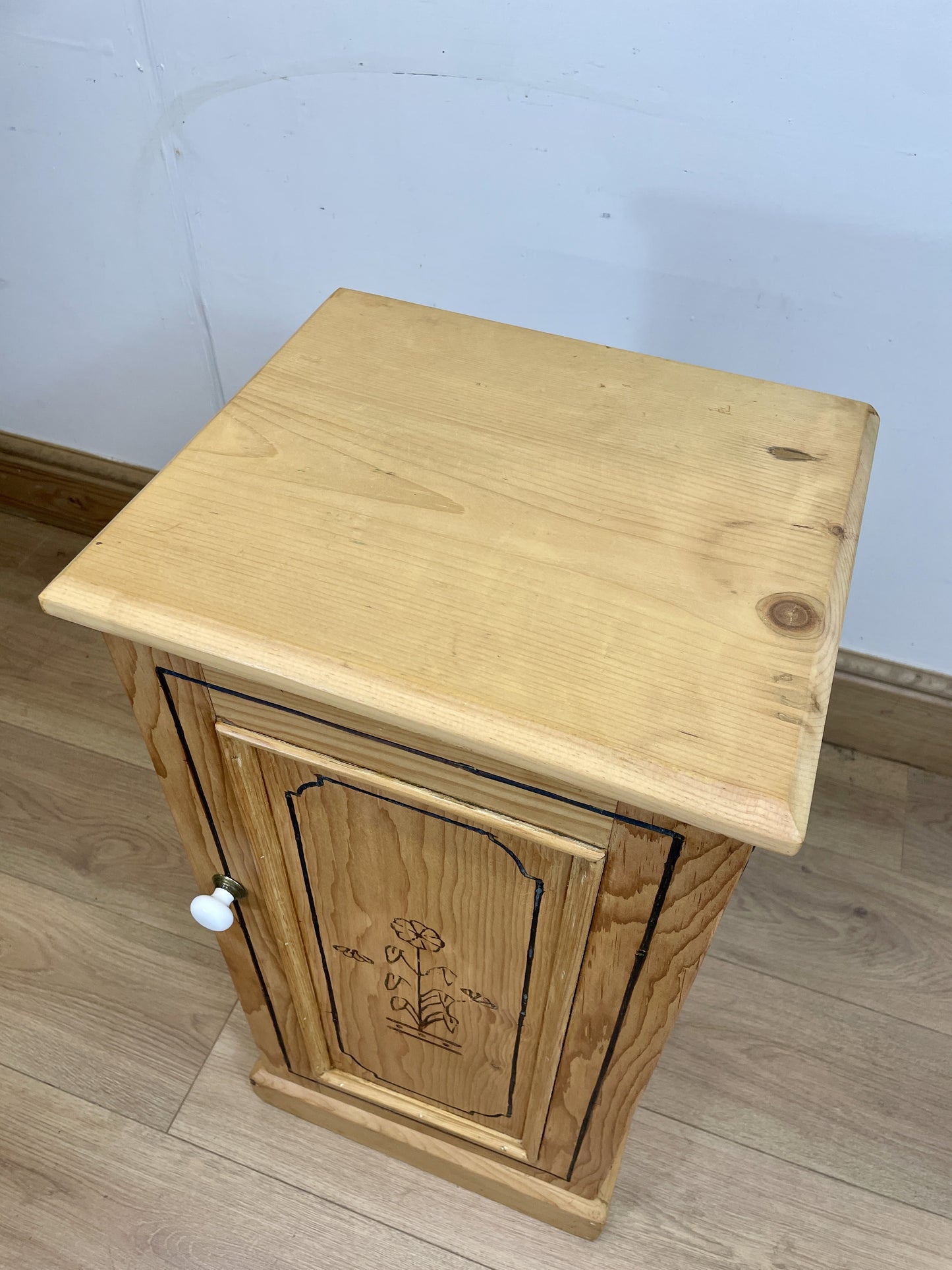 Wooden cabinet with a small door on a light wooden floor against a light blue wall.