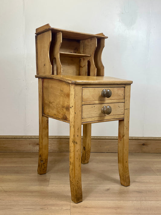 Wooden side table with a drawer on a wooden floor against a white wall