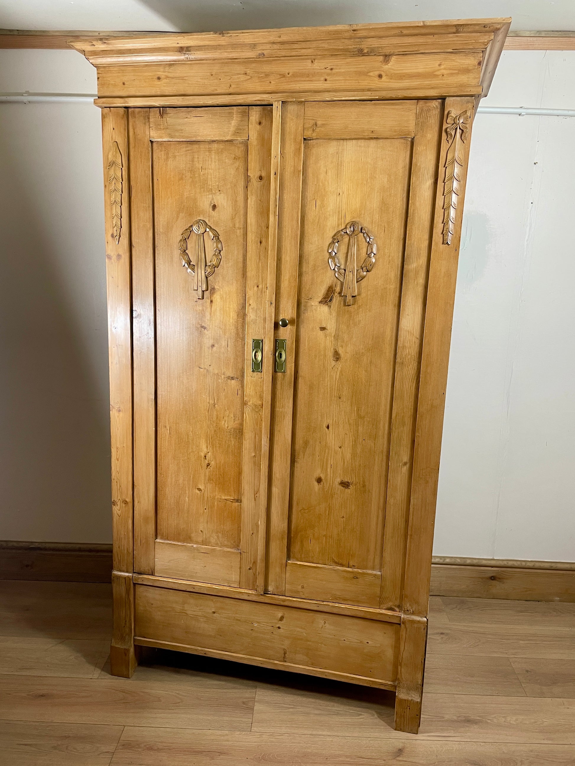Wooden wardrobe with decorative elements on a wooden floor against a white wall.
