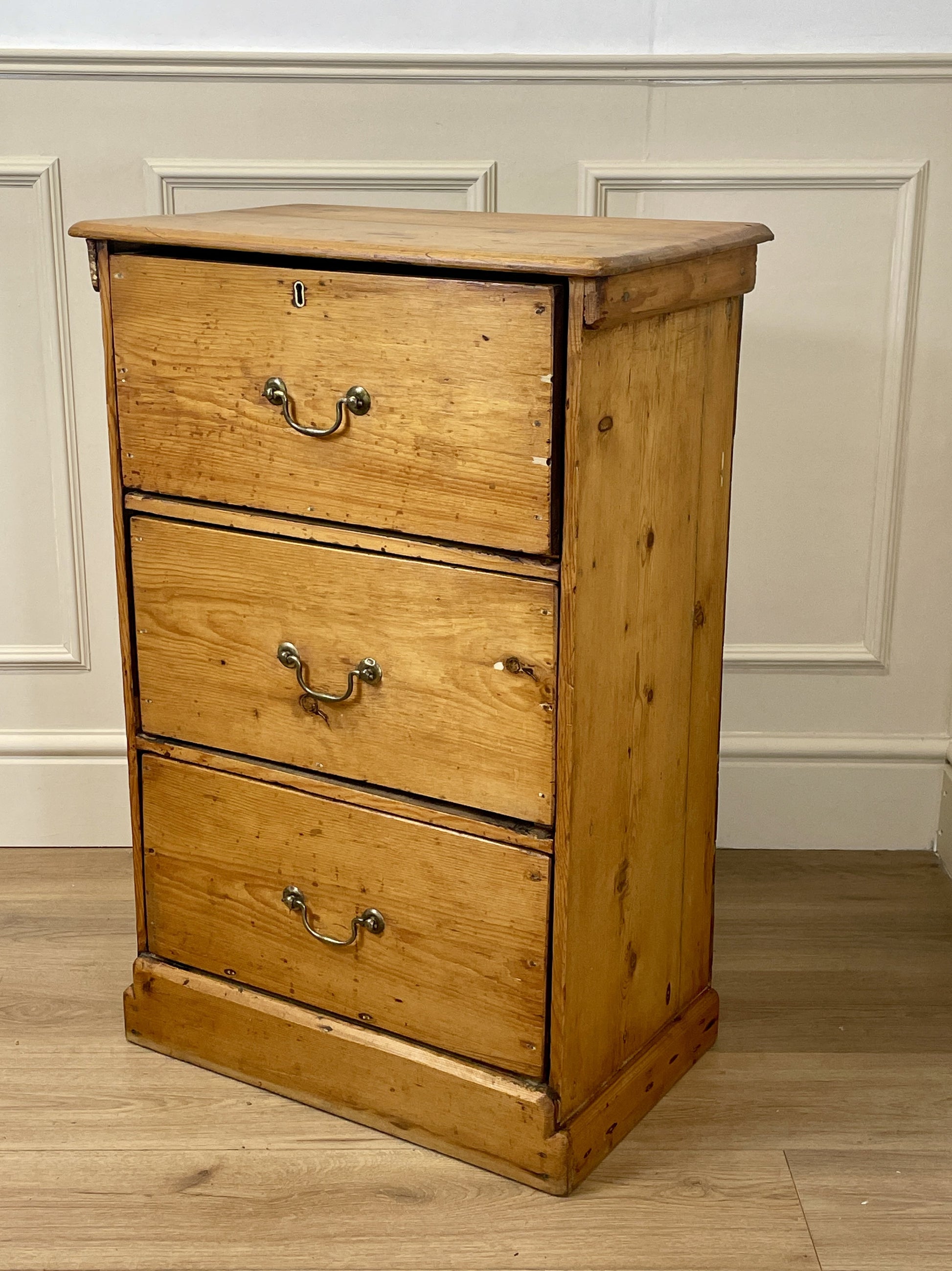 Wooden dresser with three drawers against a white paneled wall.