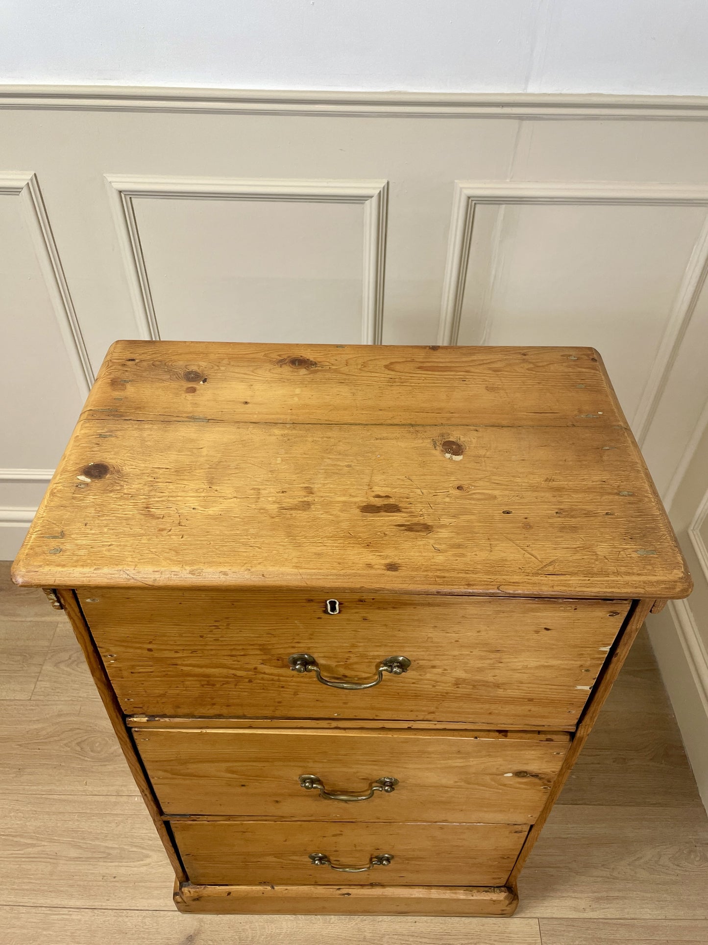 Wooden dresser with three drawers against a white paneled wall.