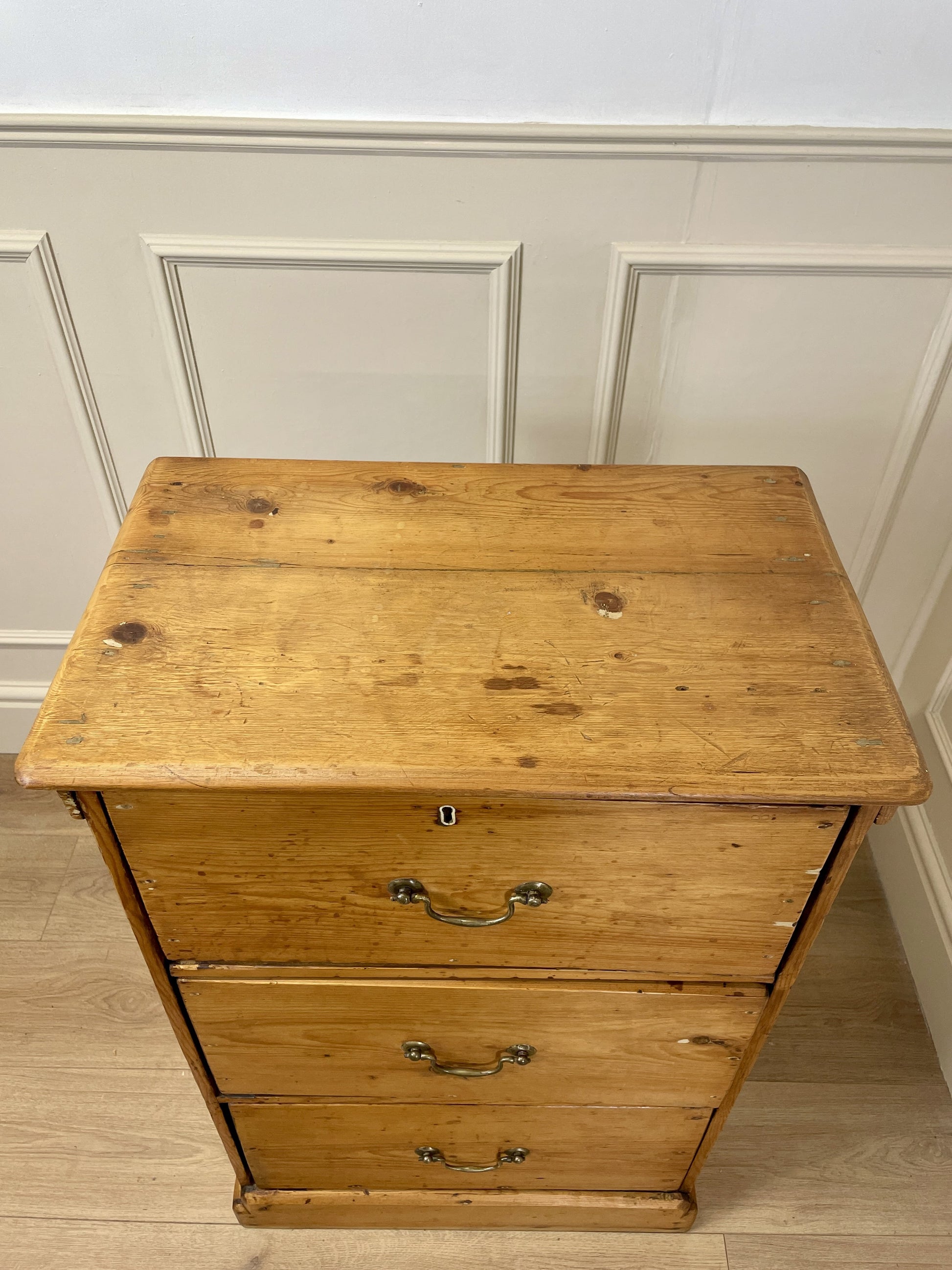 Wooden dresser with three drawers against a white paneled wall.