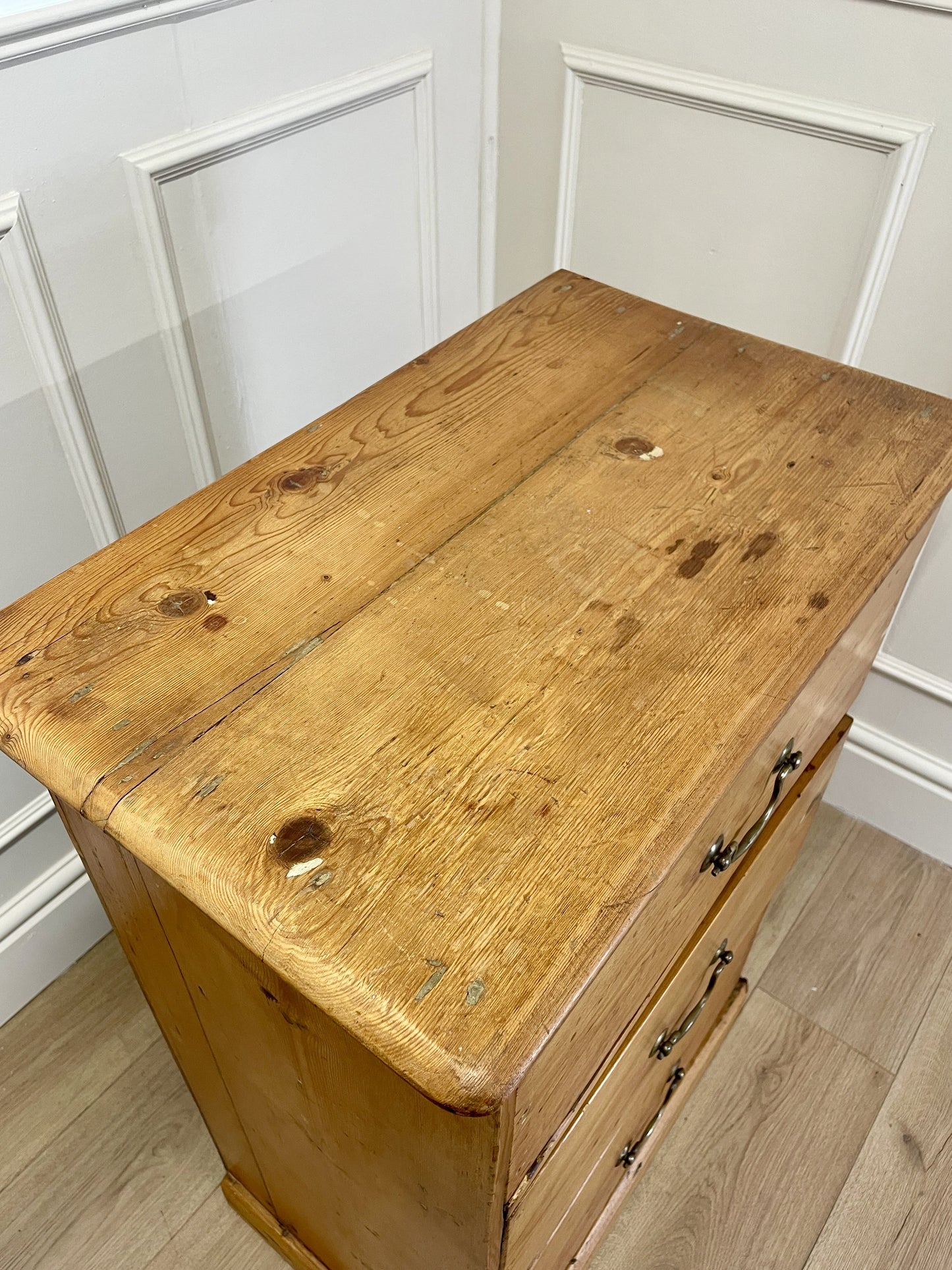 Wooden dresser with a worn surface against a white paneled wall.