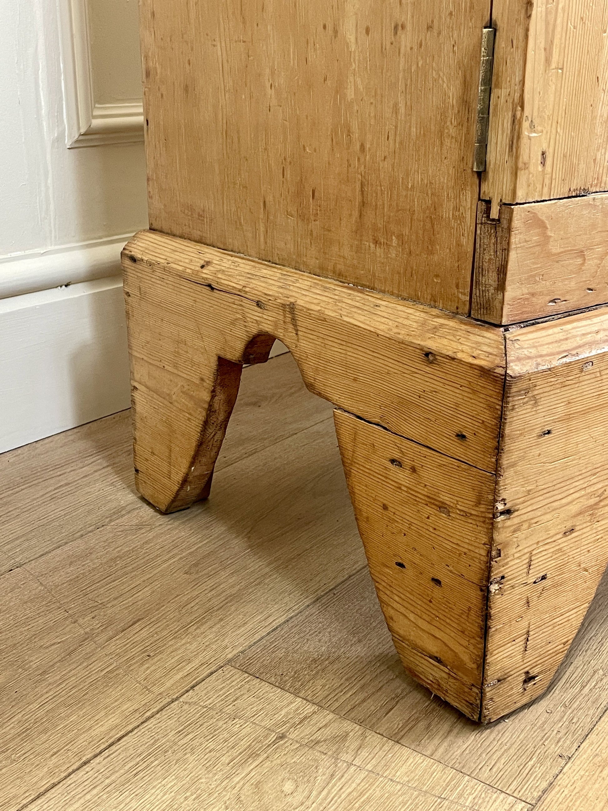 Close-up of a wooden cabinet with a unique base design on a wooden floor.